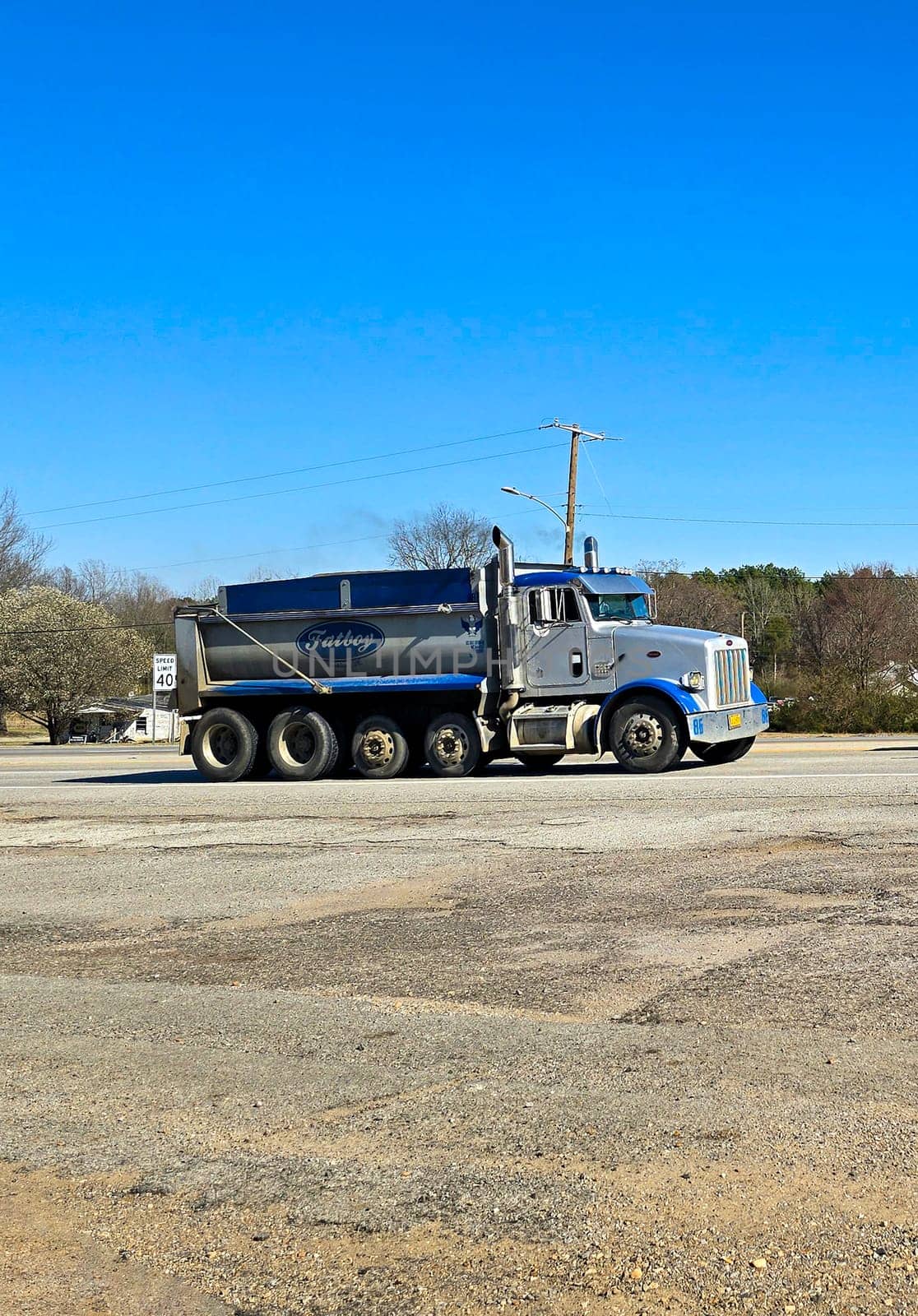 Freight liner Semi-Truck Driving on Open Highway in a Rural Area, CDL Truck America, semi truck and trailer travels along an open road under a blue sky in a rustic rural setting, showcasing commercial transportation, logistics efficiency, and professional trucking