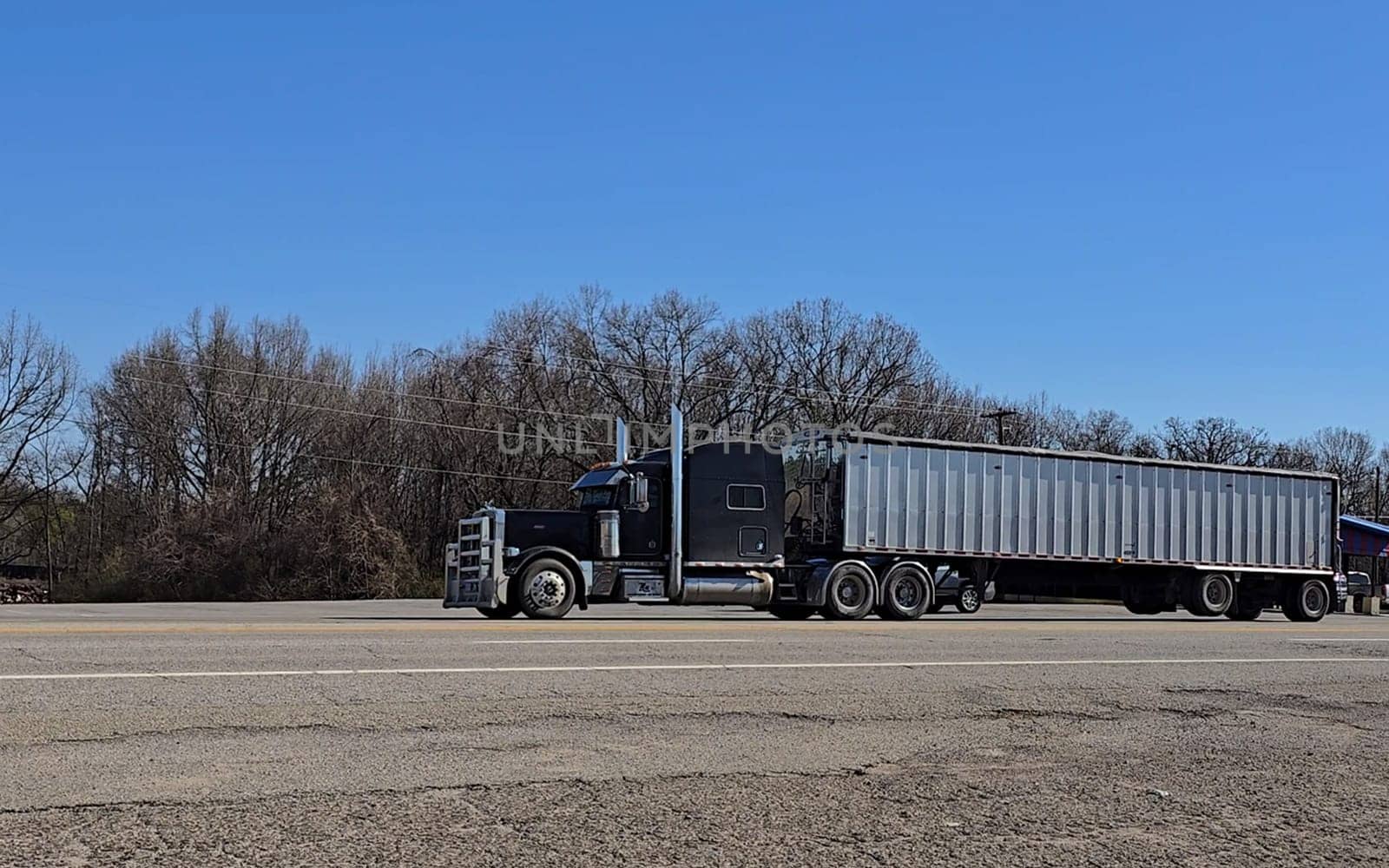 Freight liner Semi-Truck Driving on Open Highway in a Rural Area, CDL Truck America, semi truck and trailer travels along an open road under a blue sky in a rustic rural setting, showcasing commercial transportation, logistics efficiency, and professional trucking