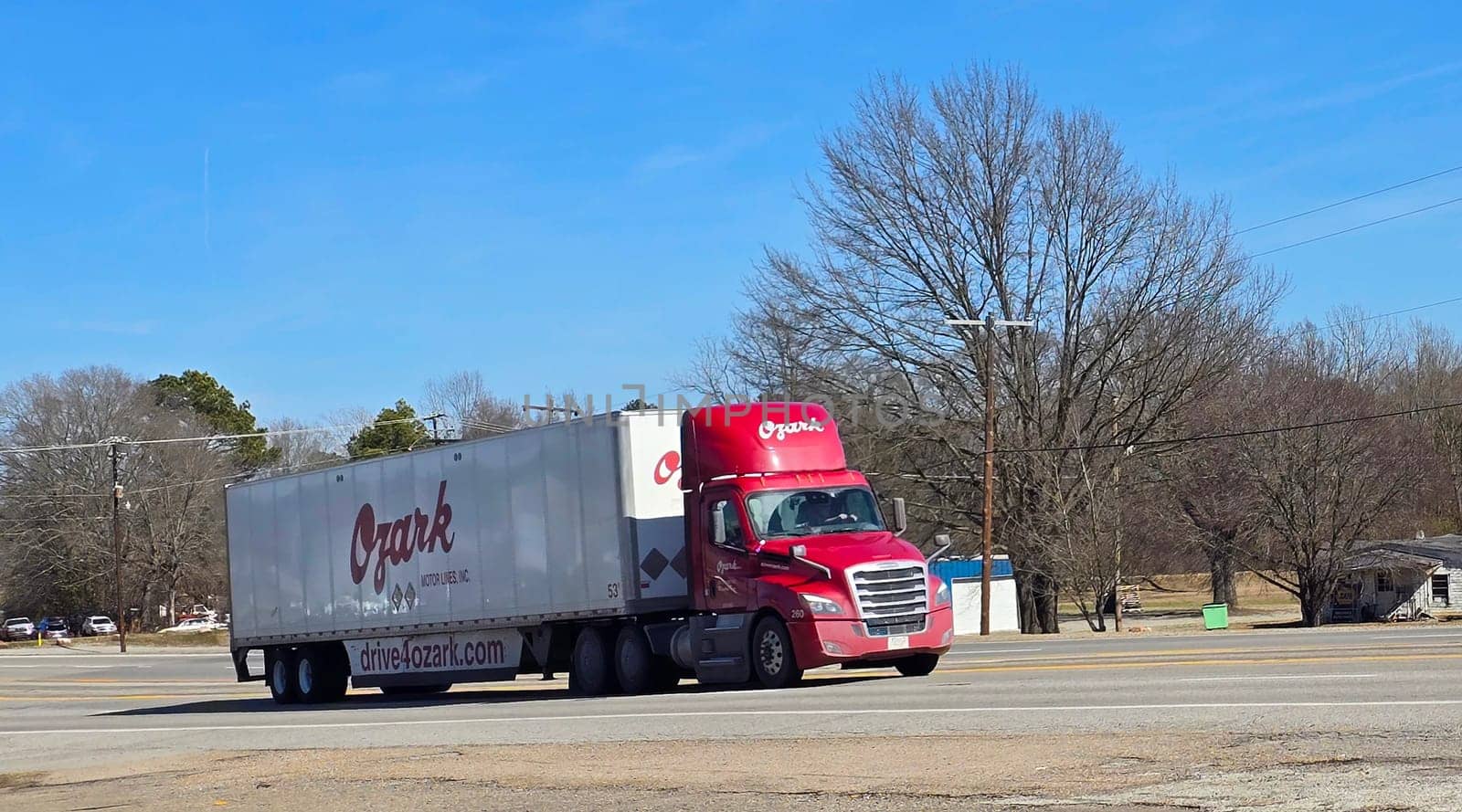 Freight liner Semi-Truck Driving on Open Highway in a Rural Area, CDL Truck America, semi truck and trailer travels along an open road under a blue sky in a rustic rural setting, showcasing commercial transportation, logistics efficiency, and professional trucking