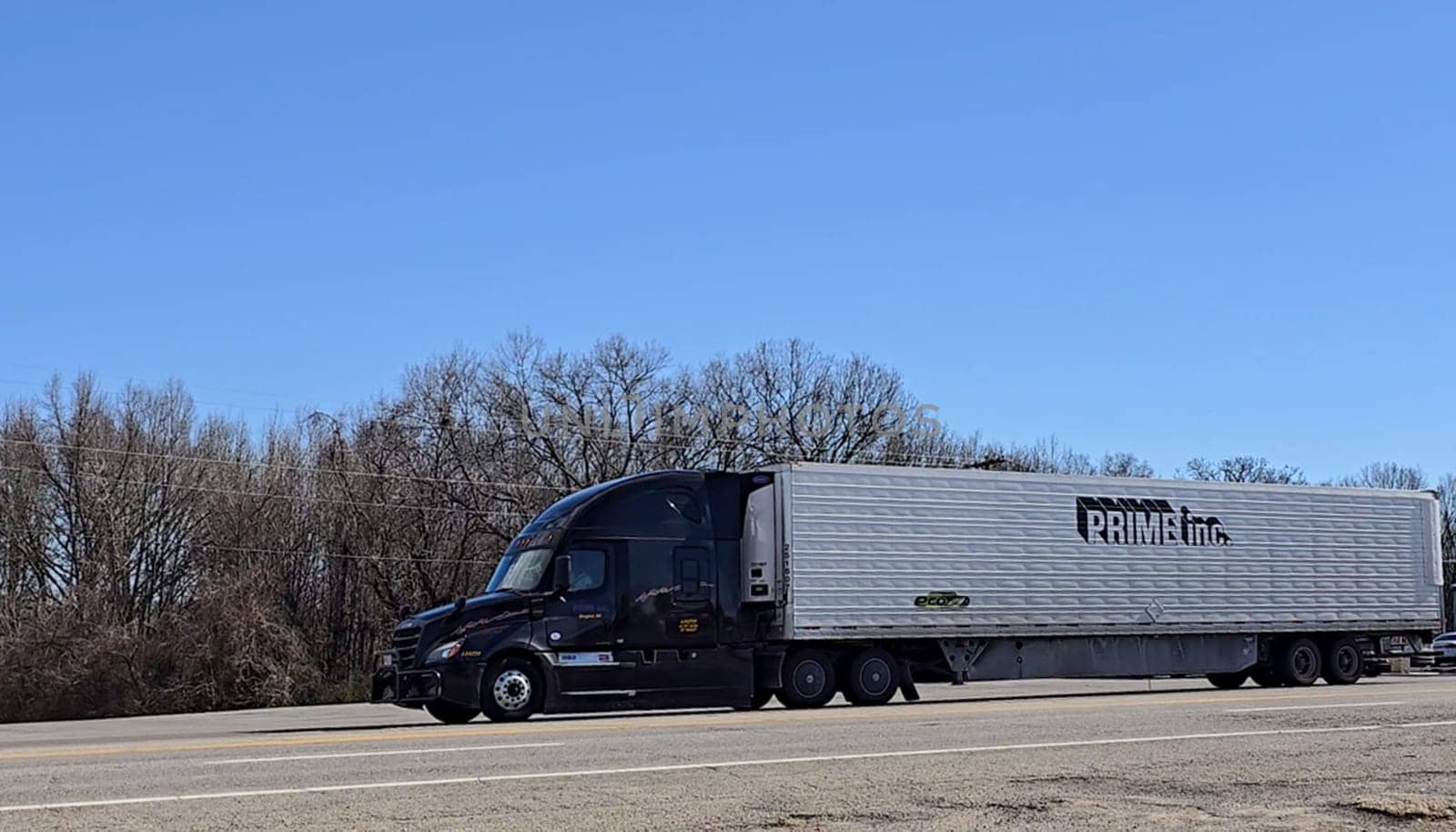 Freight liner Semi-Truck Driving on Open Highway in a Rural Area, CDL Truck America, semi truck and trailer travels along an open road under a blue sky in a rustic rural setting, showcasing commercial transportation, logistics efficiency, and professional trucking
