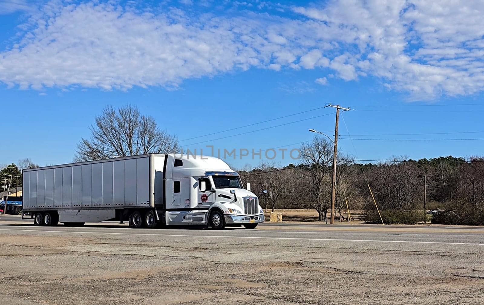 Freight liner Semi-Truck Driving on Open Highway in a Rural Area, CDL Truck America, semi truck and trailer travels along an open road under a blue sky in a rustic rural setting, showcasing commercial transportation, logistics efficiency, and professional trucking