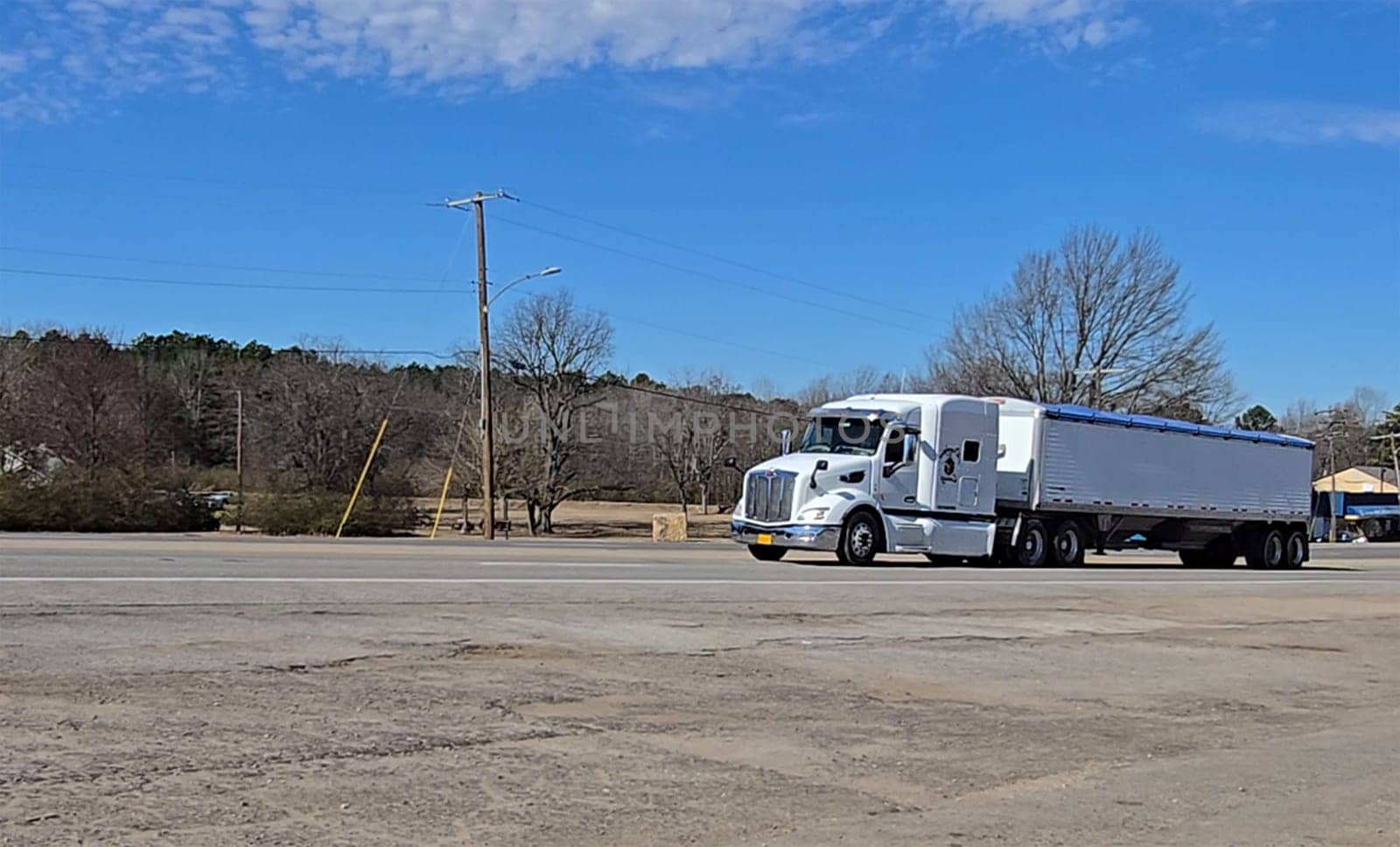 Freight liner Semi-Truck Driving on Open Highway in a Rural Area, CDL Truck America, semi truck and trailer travels along an open road under a blue sky in a rustic rural setting, showcasing commercial transportation, logistics efficiency, and professional trucking