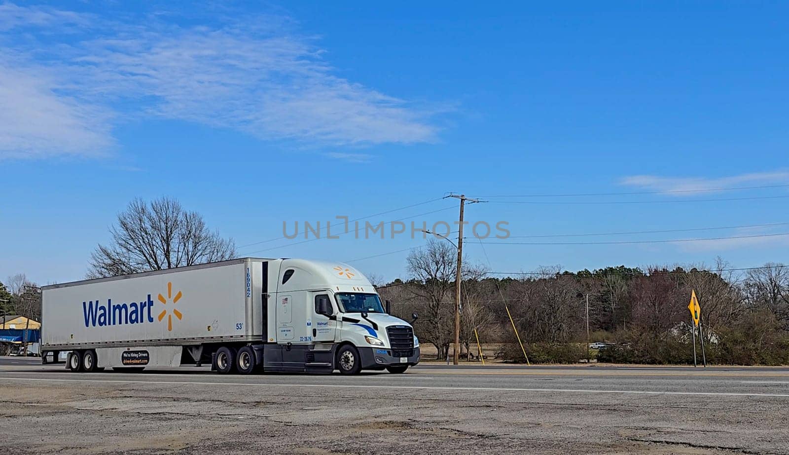 Freight liner Semi-Truck Driving on Open Highway in a Rural Area, CDL Truck America, semi truck and trailer travels along an open road under a blue sky in a rustic rural setting, showcasing commercial transportation, logistics efficiency, and professional trucking
