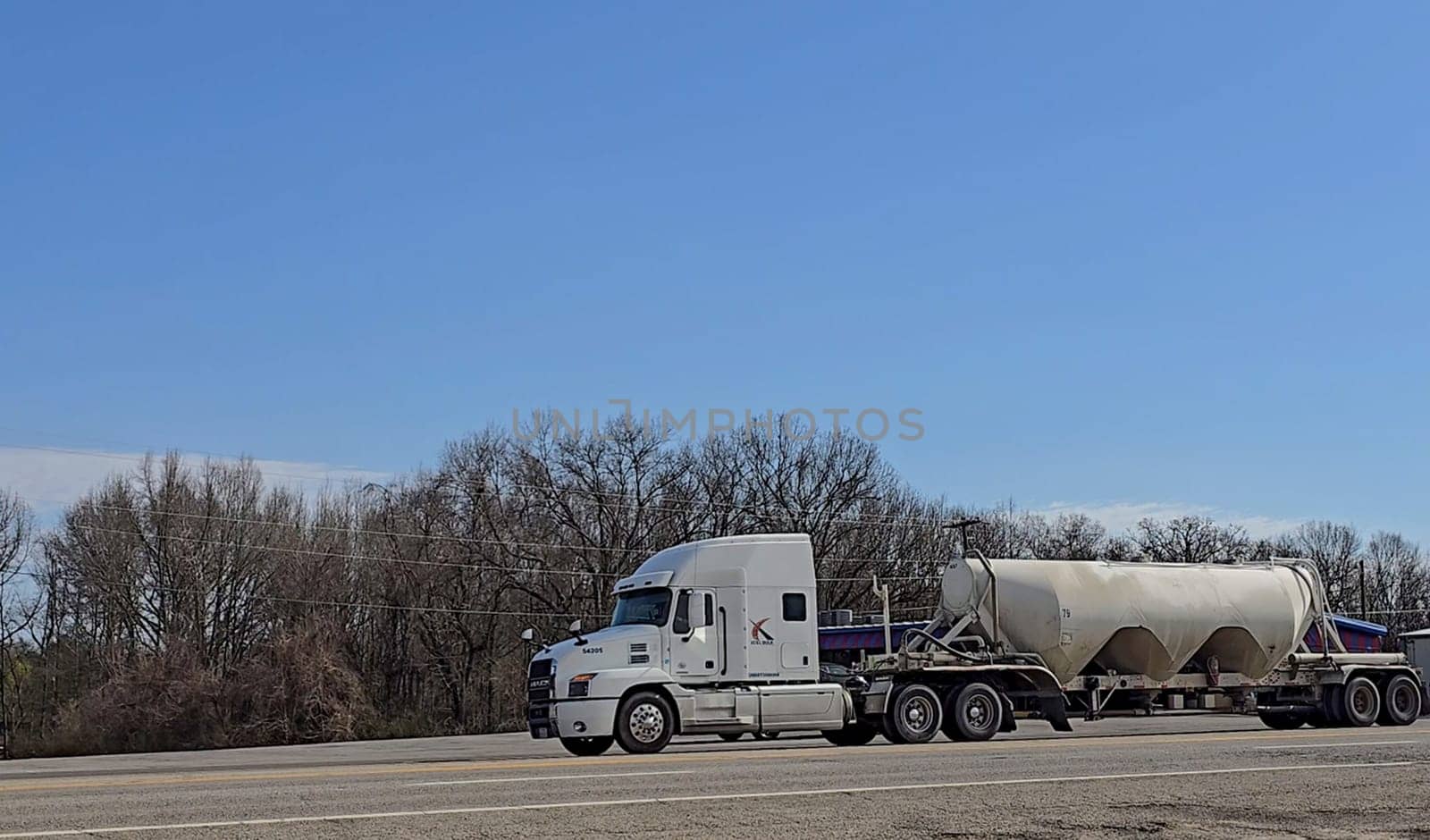 Freight liner Semi-Truck Driving on Open Highway in a Rural Area, CDL Truck America, semi truck and trailer travels along an open road under a blue sky in a rustic rural setting, showcasing commercial transportation, logistics efficiency, and professional trucking