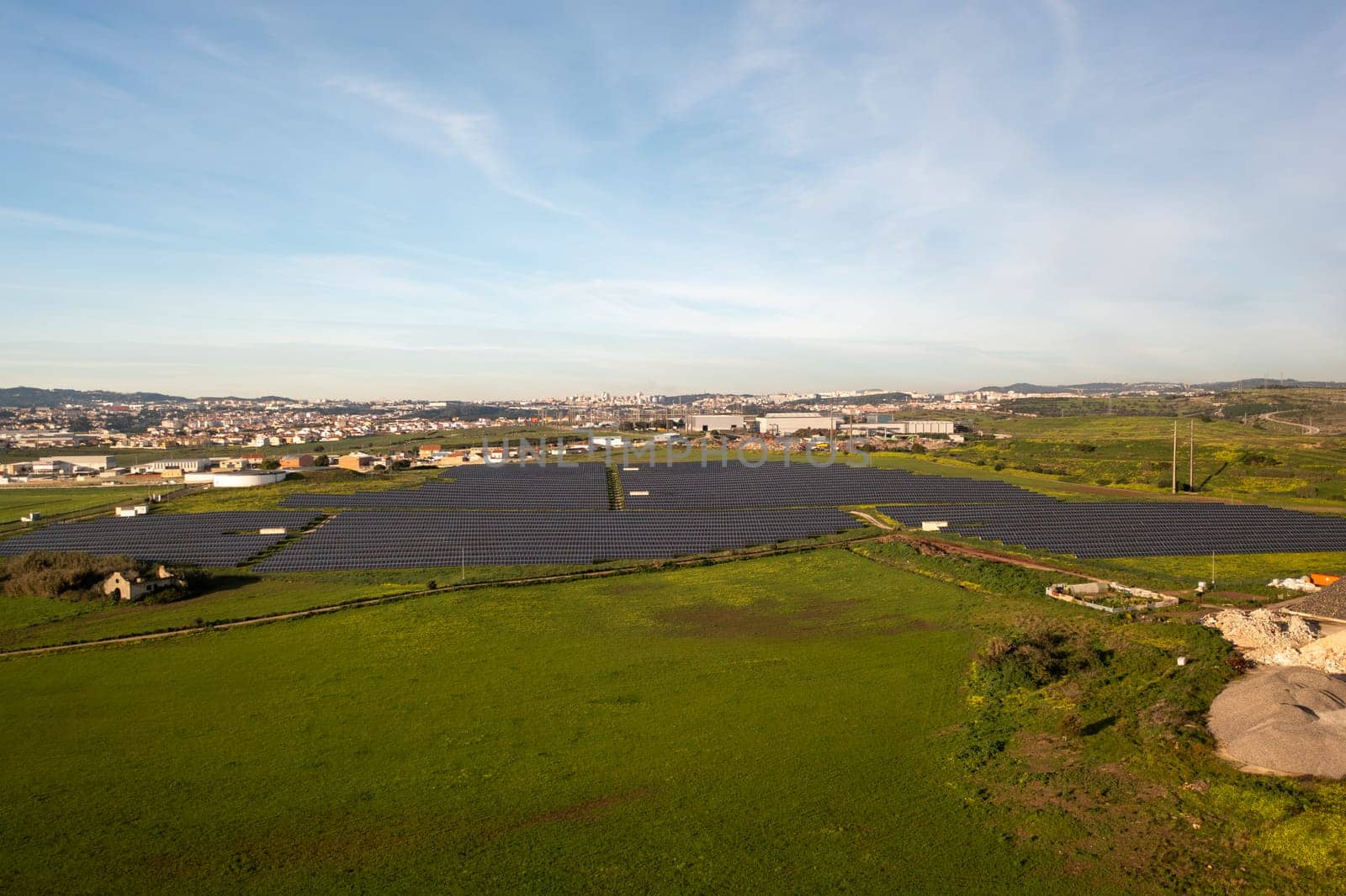Aerial shot of solar panels in field, vast landscape with green energy and townscape in distance under clear sky during daytime