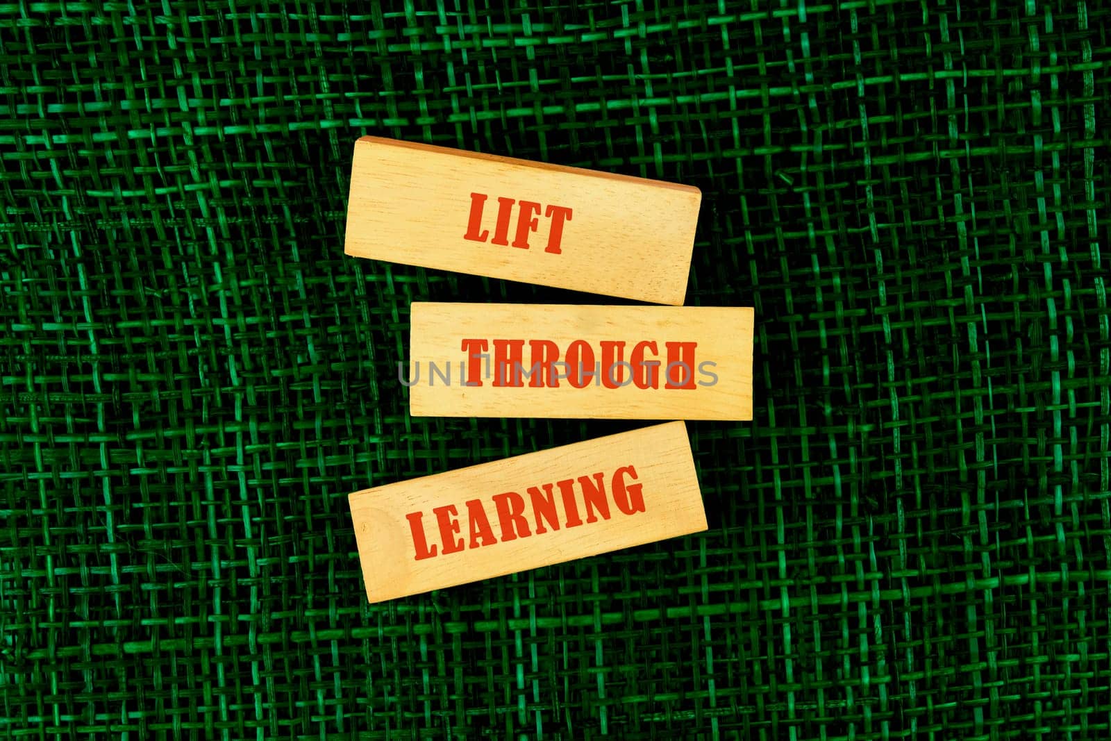 Wooden blocks with the words lift through learning placed on a textured green surface, symbolizing the importance of education and growth
