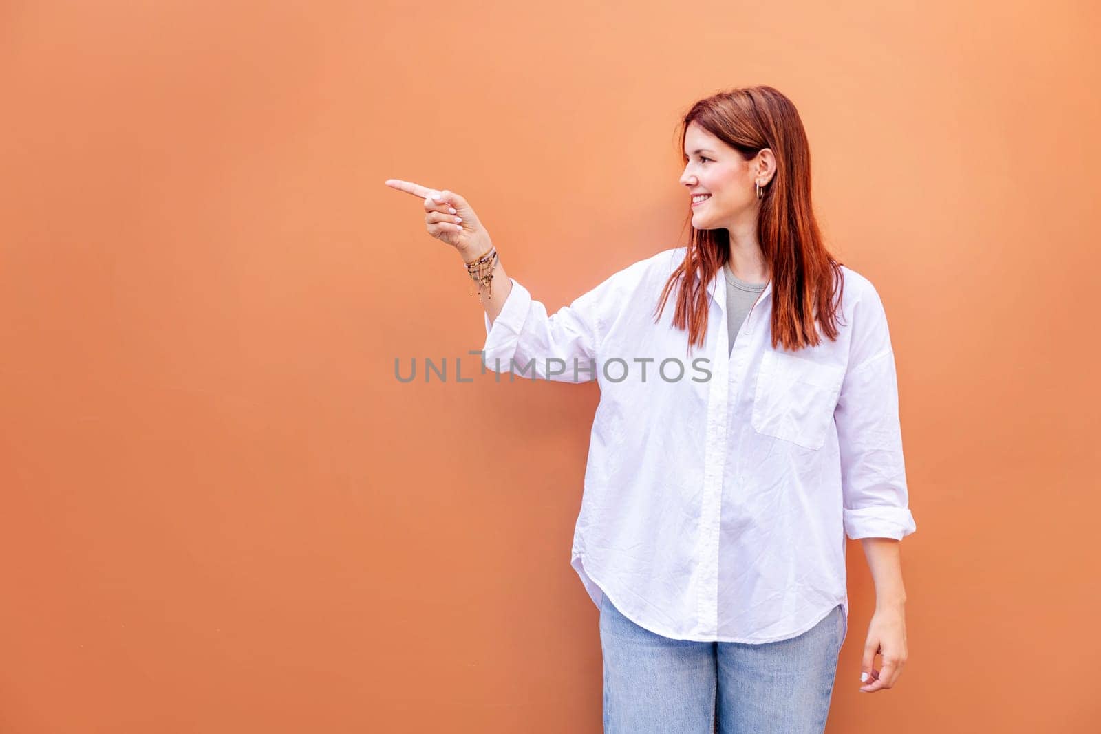 smiling young woman in white shirt and blue jeans is pointing to the side, copyspace for text