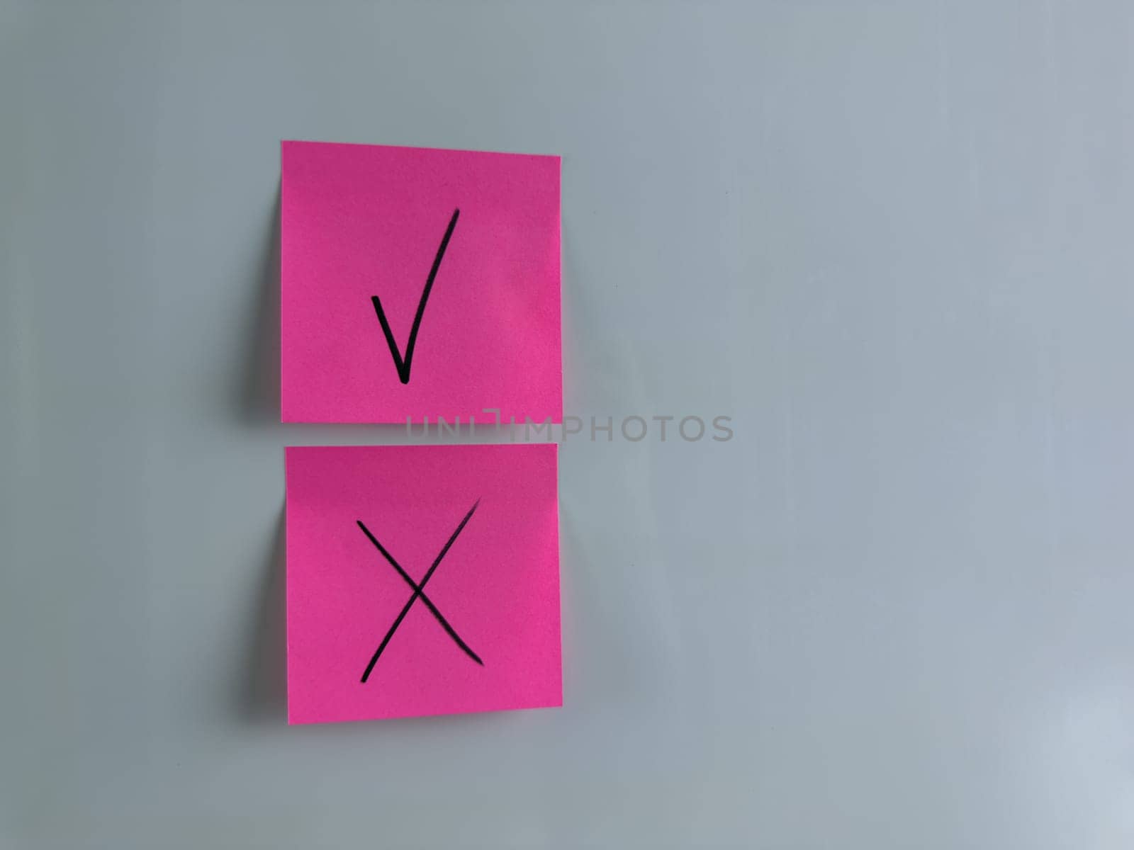 Making management decision in company and marking important choice with special symbols. Sticky note on white background with check mark and cross to indicate choice and decision