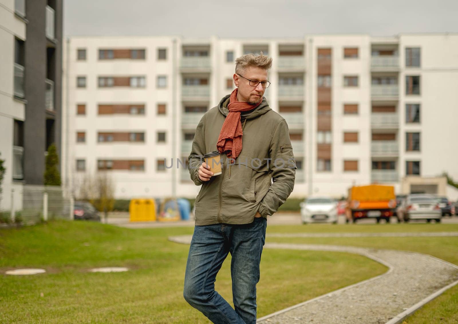 Young Attractive Man Walks With A Cup Of Coffee Near An Apartment Building