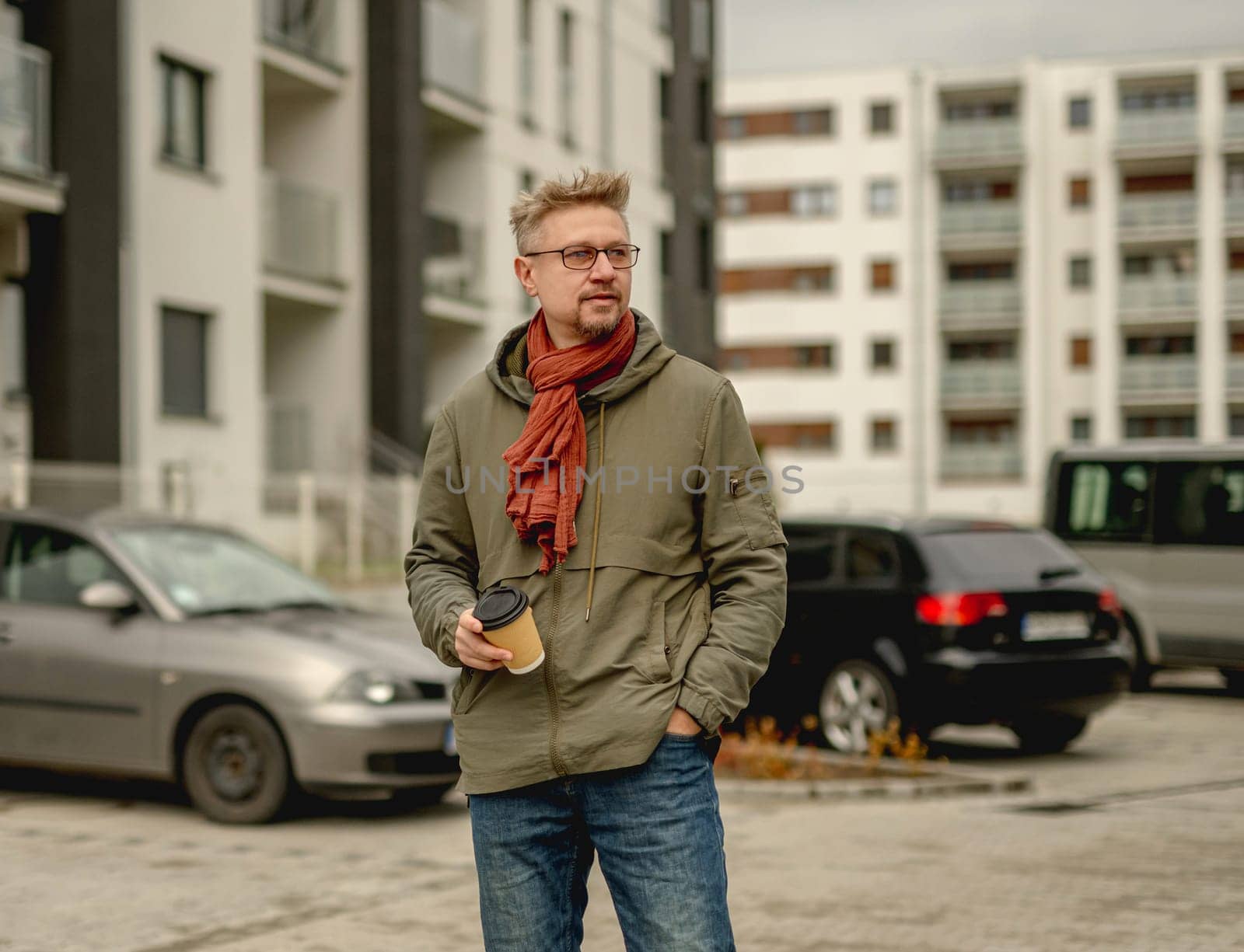 Young Attractive Man Waits On A Street With Coffee In The Courtyard Of An Apartment Building