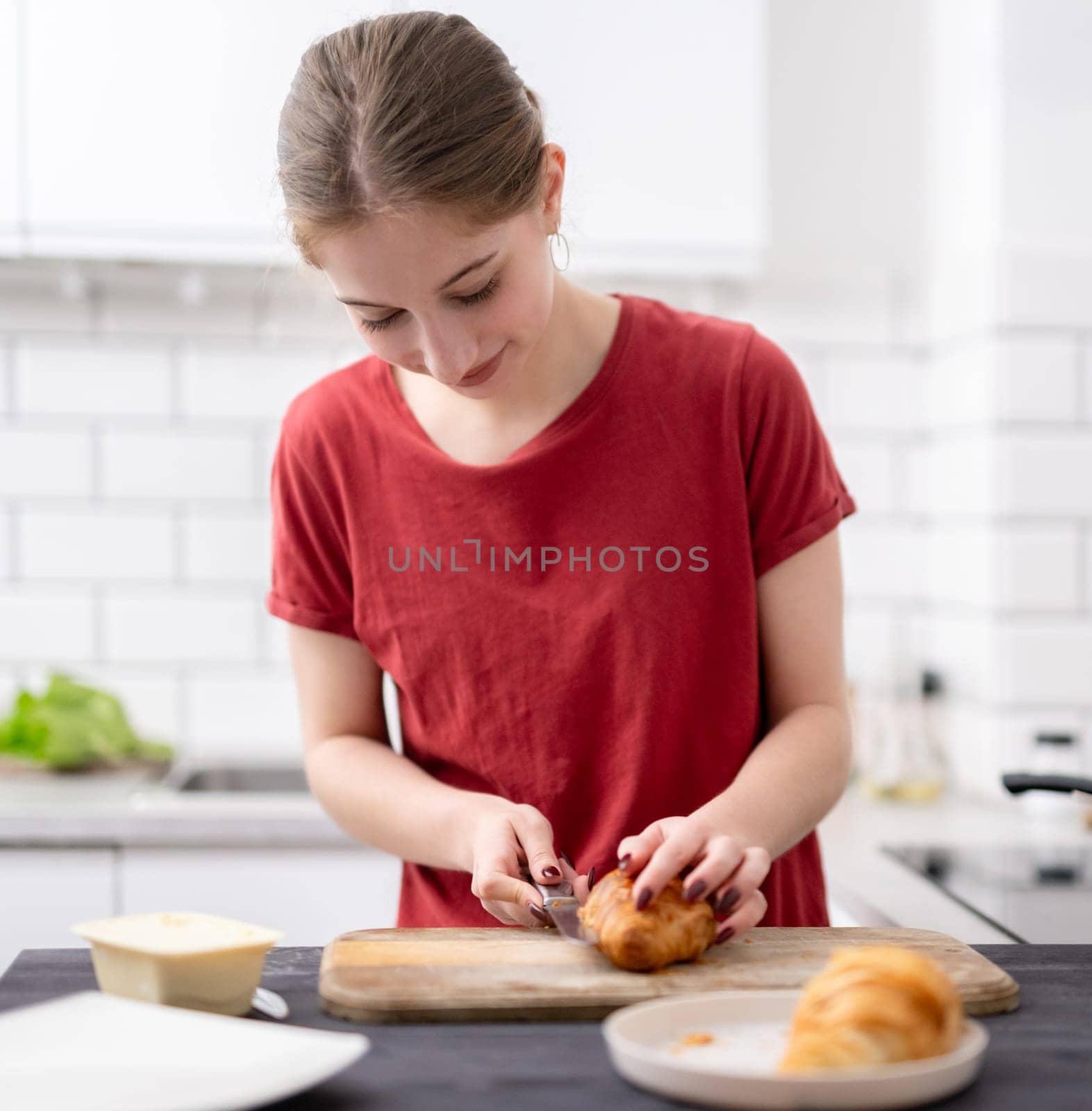 Pretty Young Girl Cuts A Croissant For Breakfast