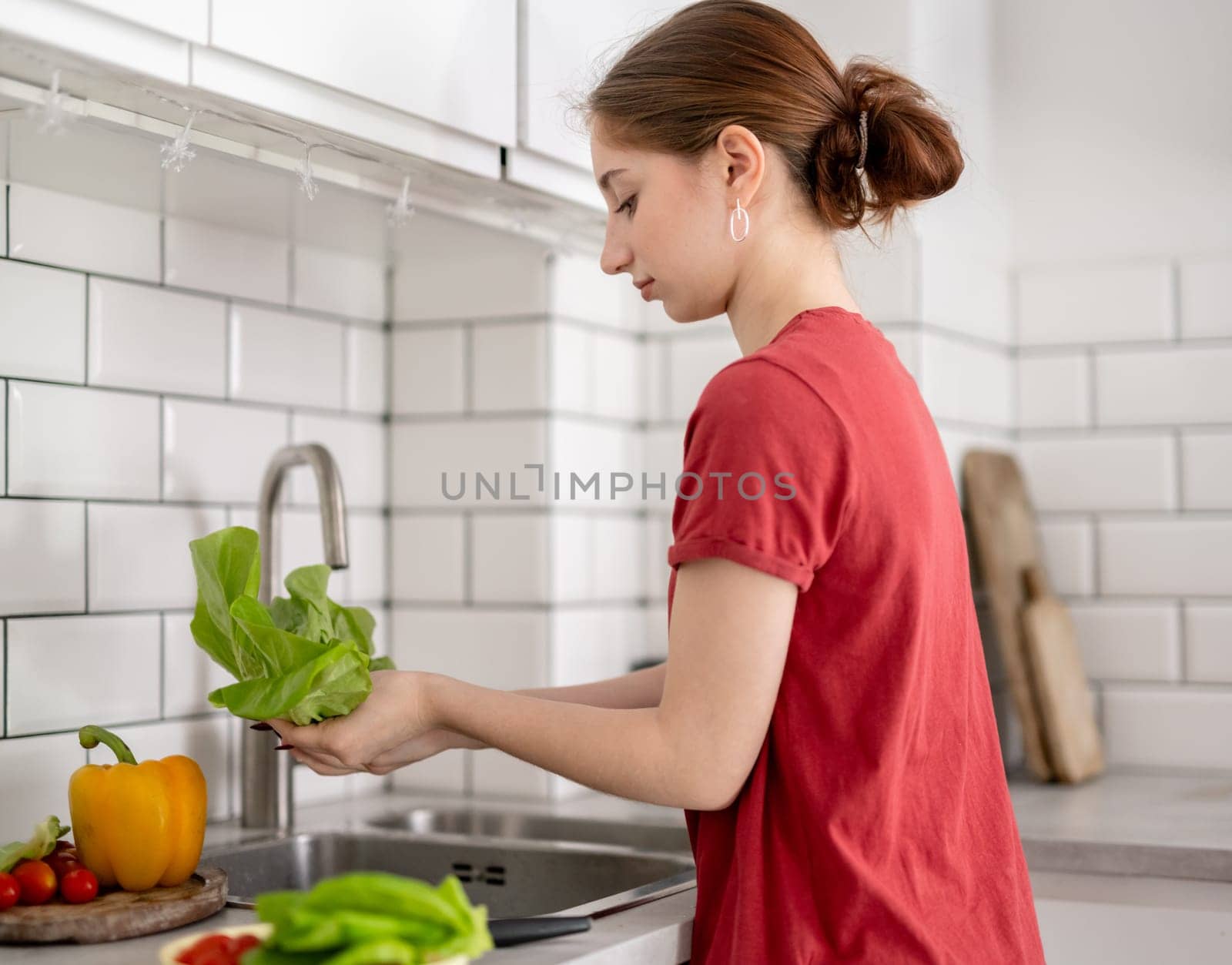 Young Girl Washes Lettuce Leaves In The Kitchen At Home