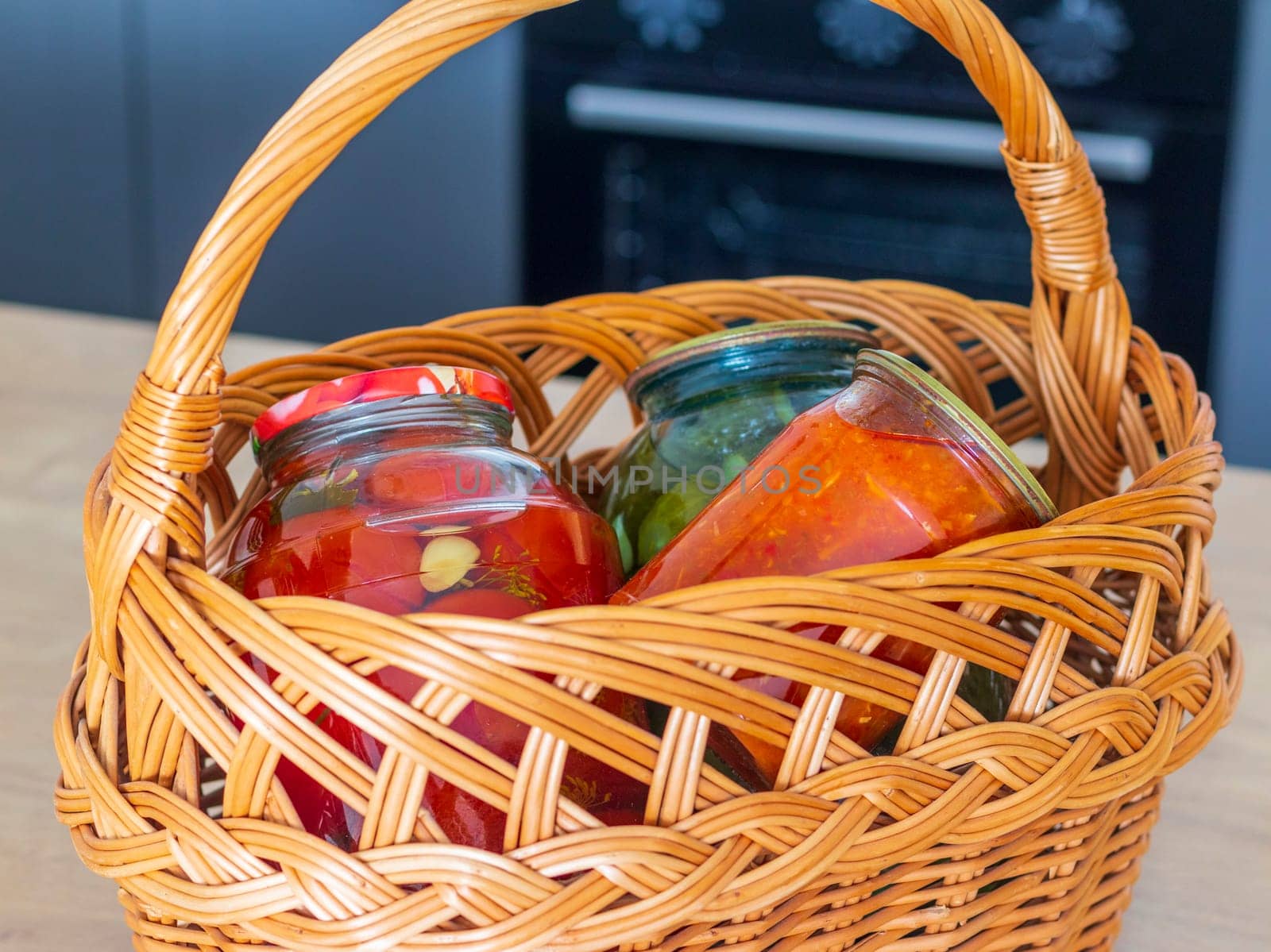 Jars with different types of pickles and preserves in a wicker basket. Food