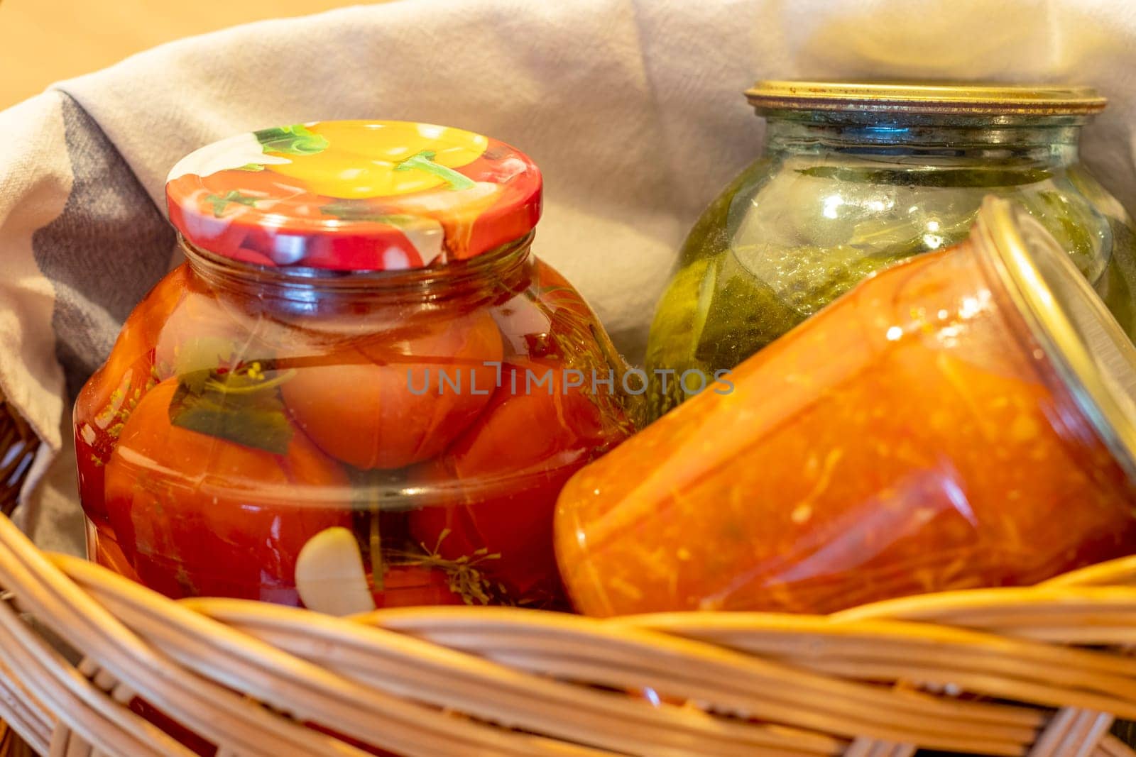 Jars with different types of pickles and preserves in a wicker basket. Food