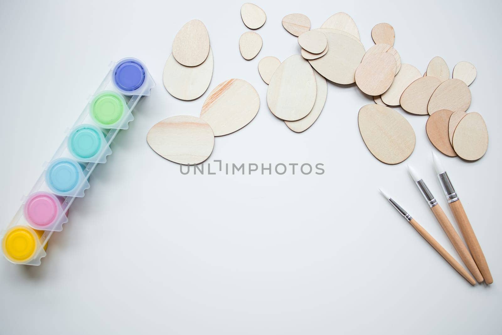 Wooden Easter egg shapes with paint and brushes with copy space for creative crafting.
