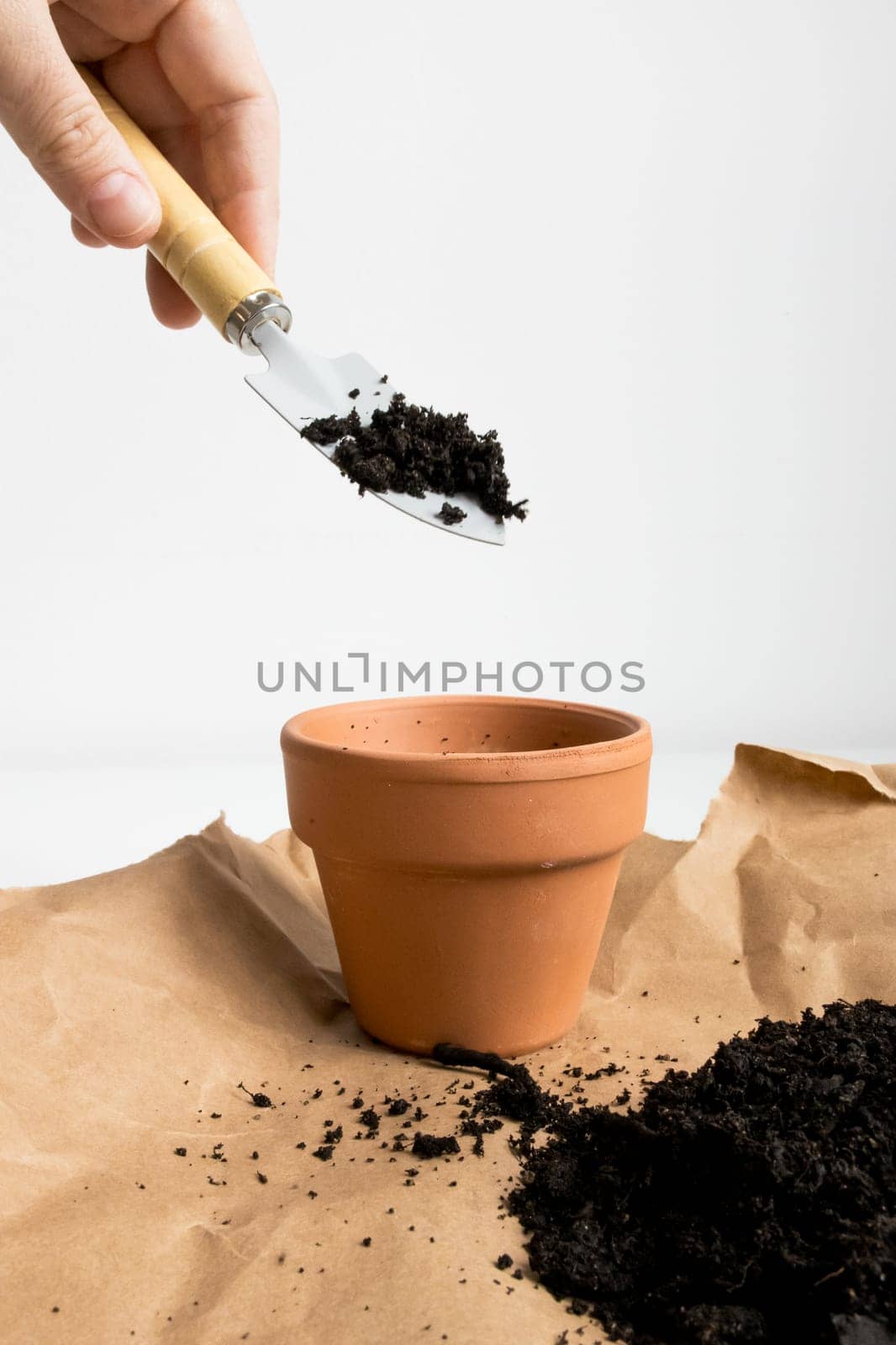 Hand pouring soil into terracotta pot on brown paper for gardening planting preparation.