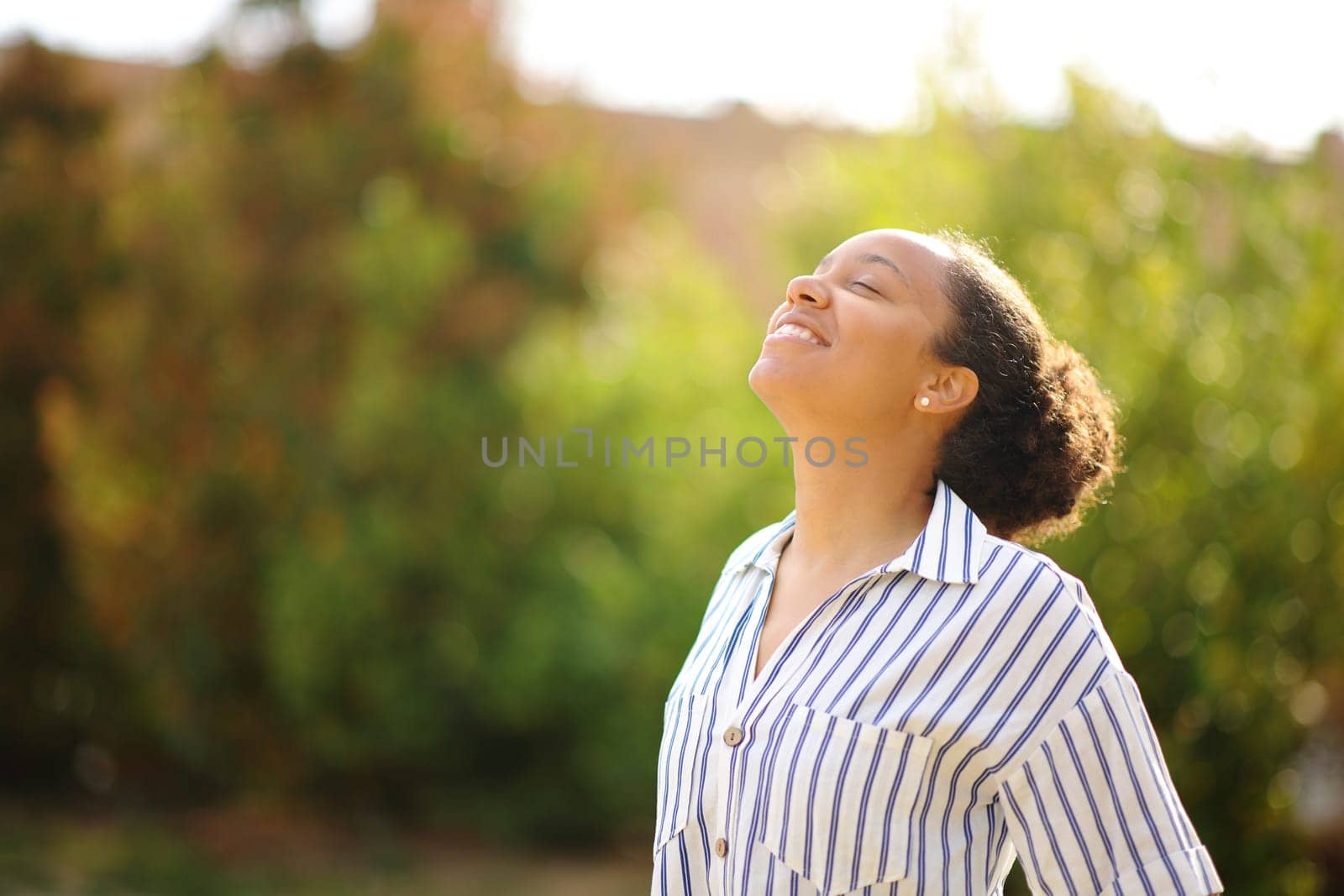 Happy black woman breathing fresh air standing in a park