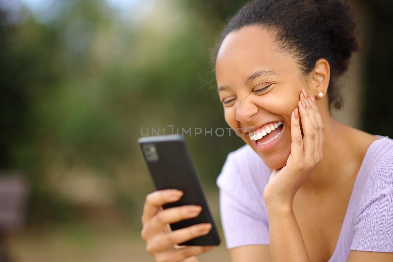 Funny black woman checking phone laughing loud in a park