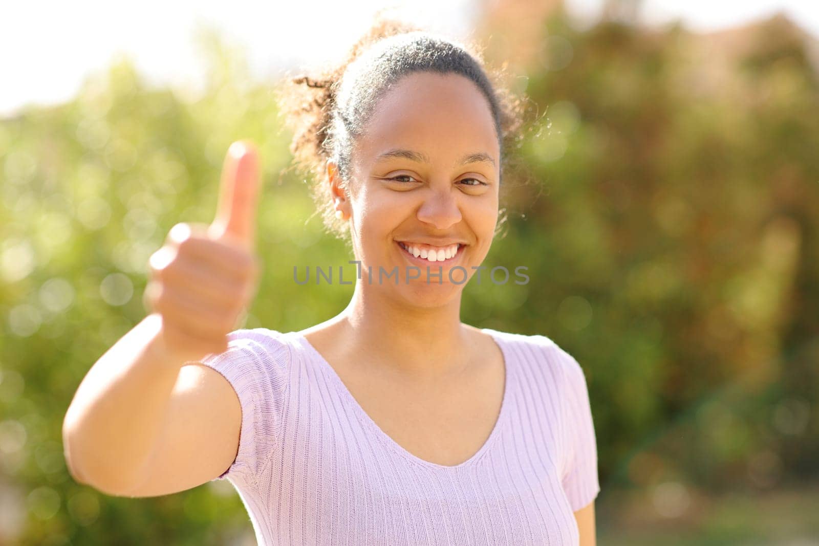 Front view portrait of a happy black woman gesturing thumbs up outdoors