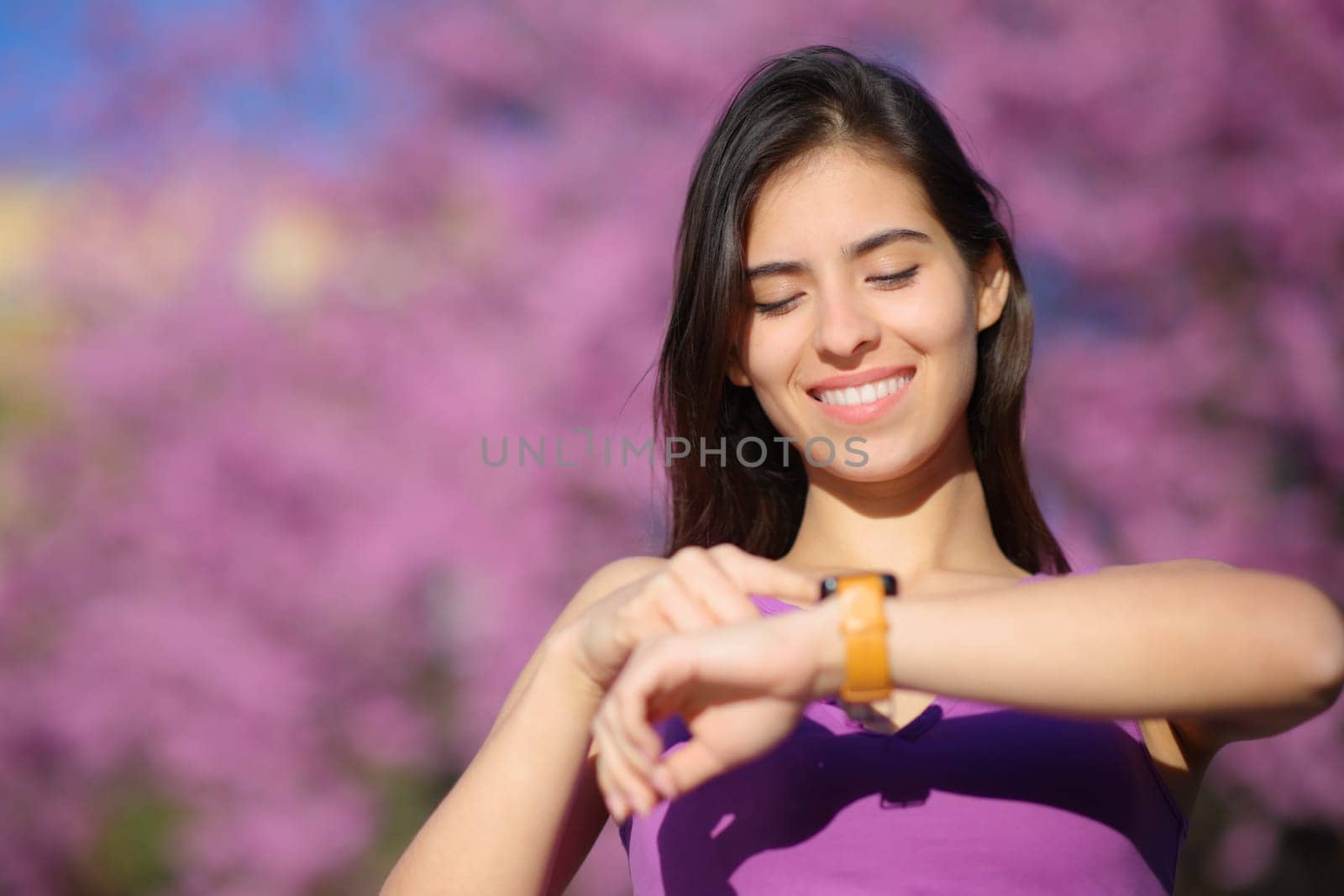 Front view portrait of a happy woman using smartwatch in a violet park