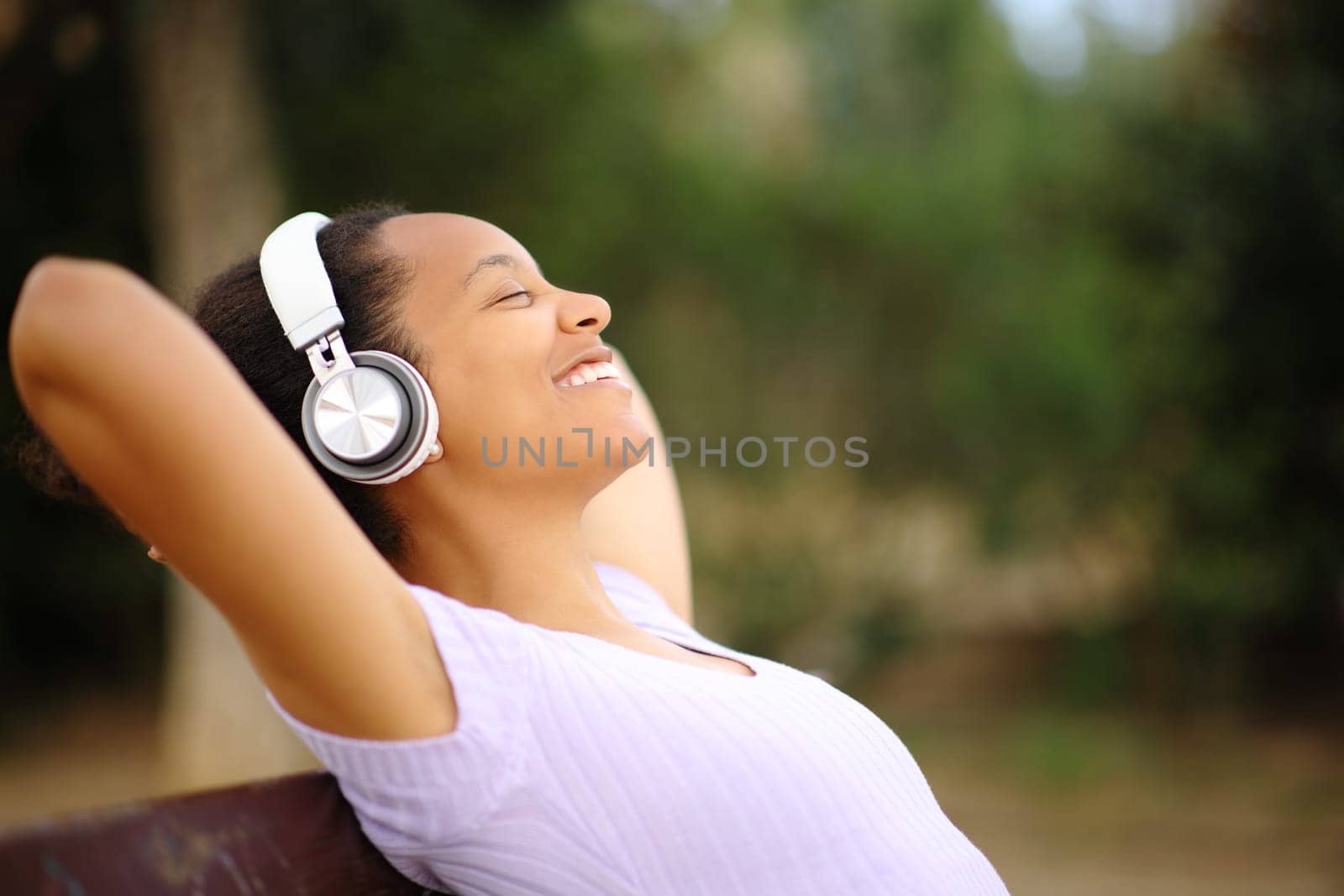 Profile of a black woman wearing headphone relaxing listening music in a park