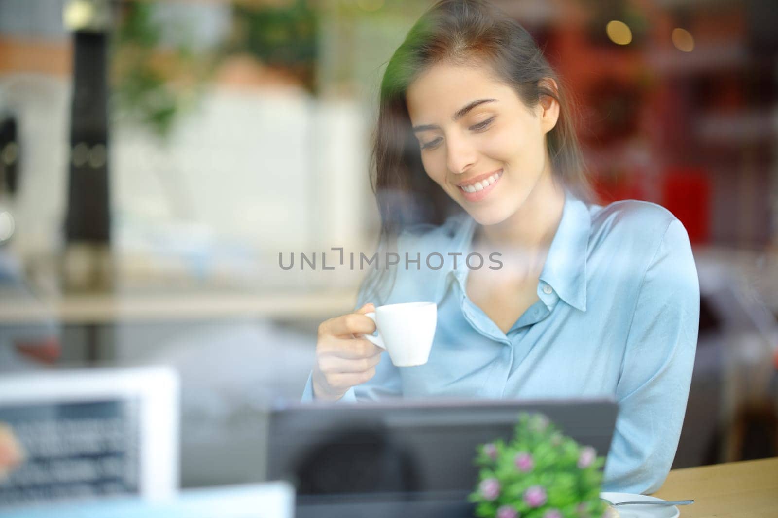 Happy woman drinking coffee in a bar using tablet