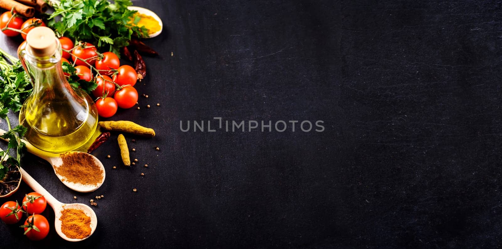 Food background. Top view of olive oil, cherry tomato, herbs and spices on rustic black slate. Colorful food ingredients border. Italian cuisine.