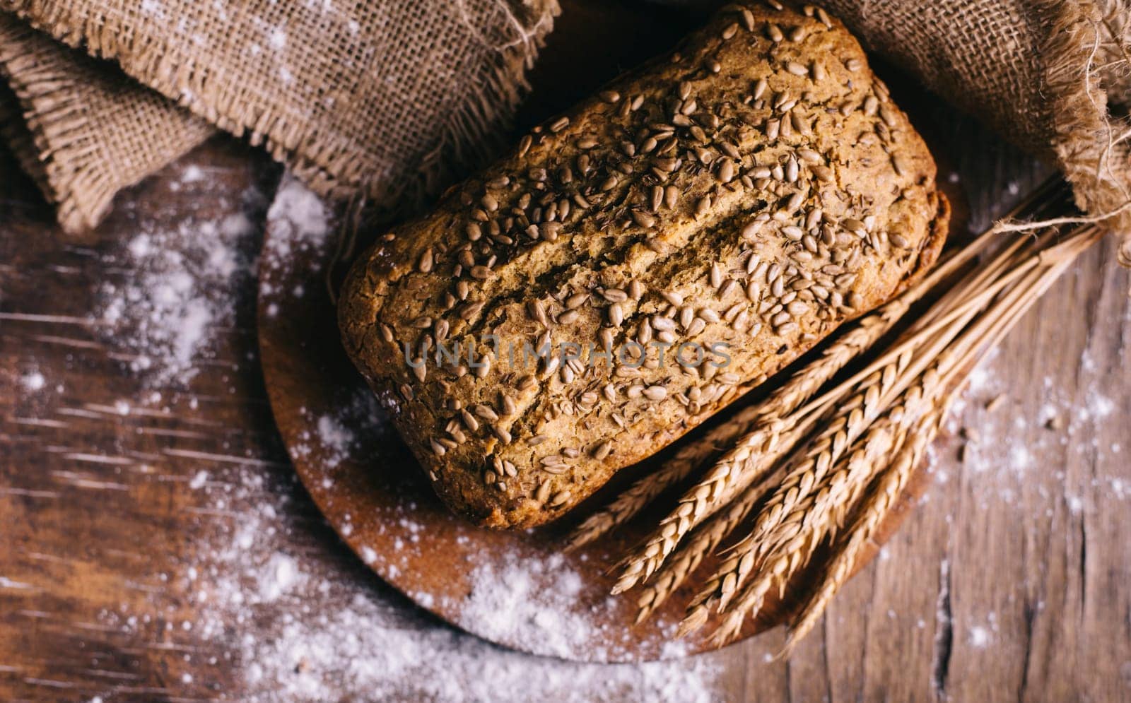 Top view of homemade bread loaf with wholegrain wheat on vintage wooden table. Organic healthy food preparation from above.