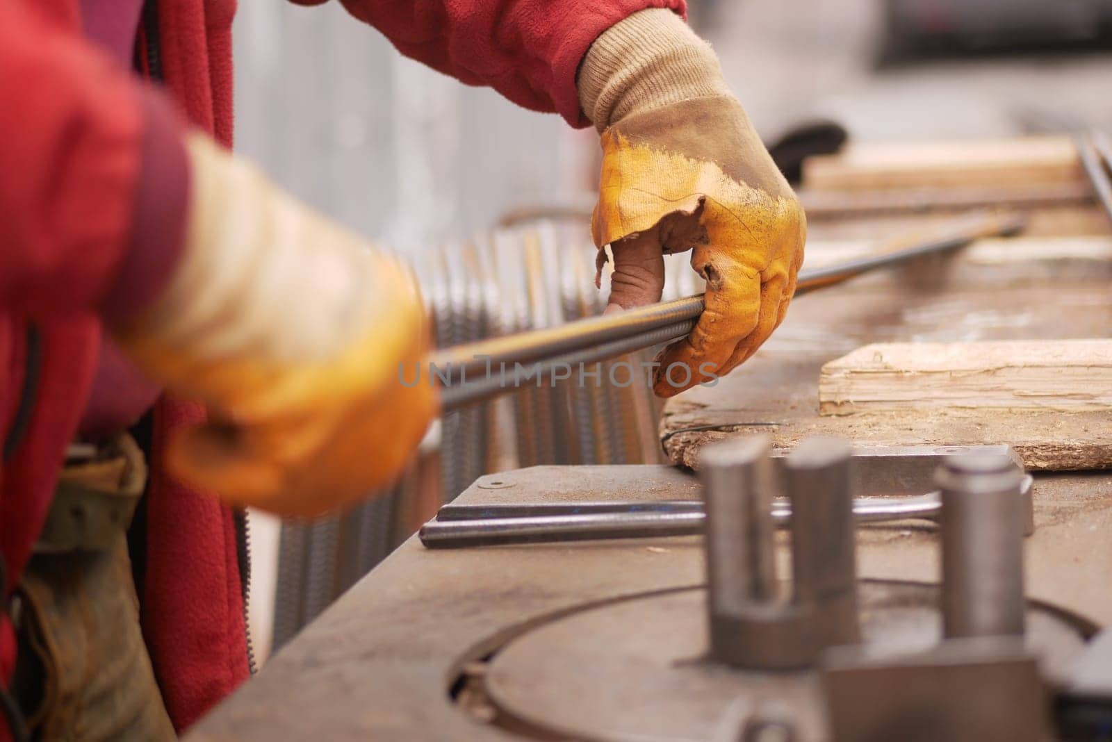 Skilled worker shapes metal rods while wearing protective gloves.