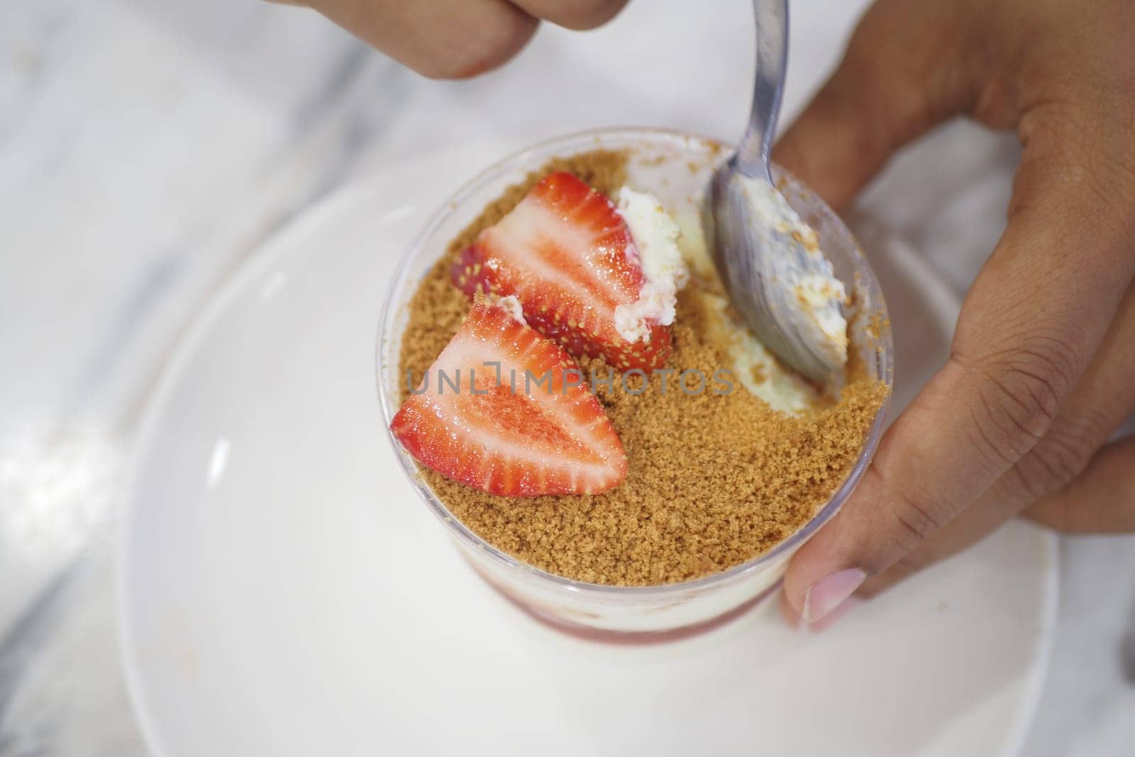 A hand holds a spoon ready to enjoy a dessert with strawberries.