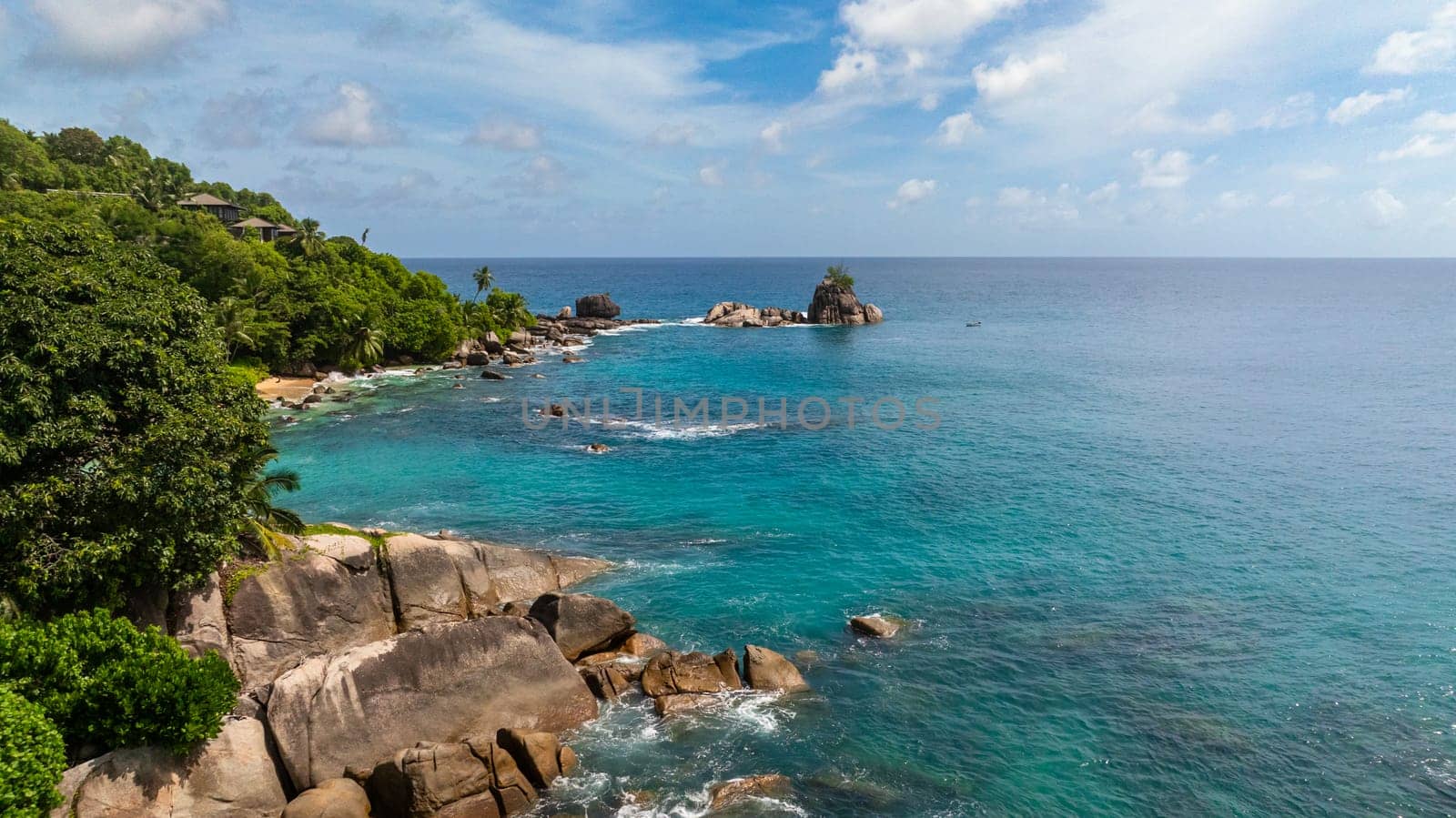 Clear turquoise water with waves hitting rocky shoreline and greenery in the background. Seychelles, Mahe.