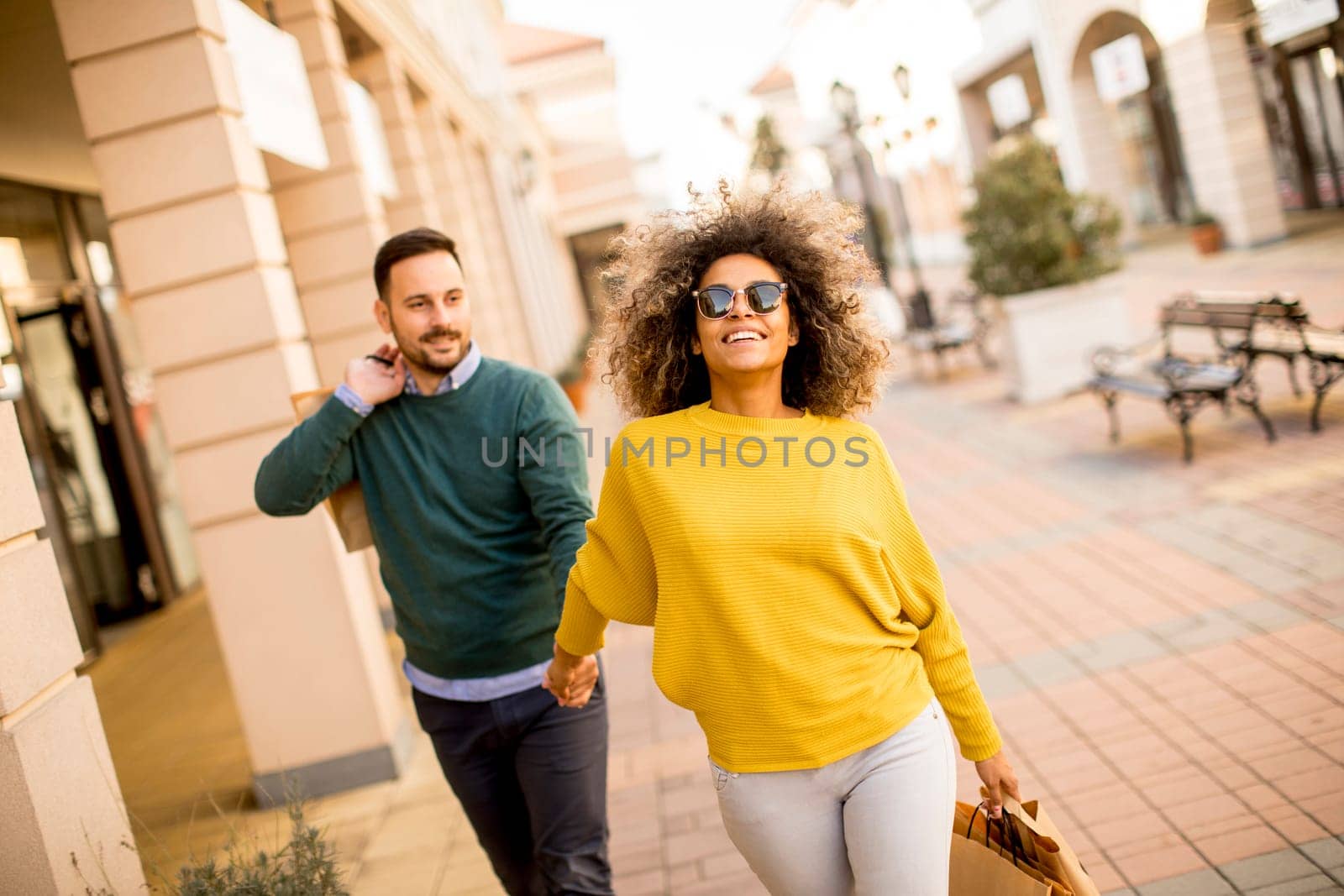 Young and cheerfull couple walking along street with shopping bags