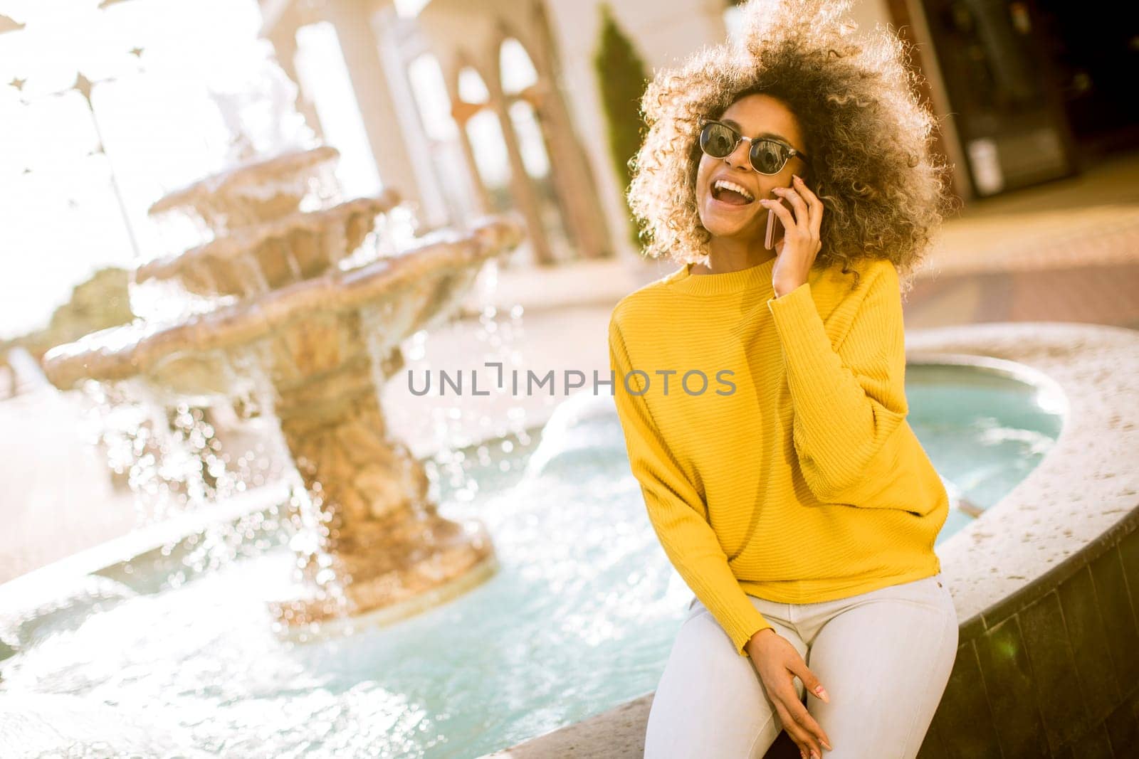 Aftican american young woman sits near fountain and talks on smartphone