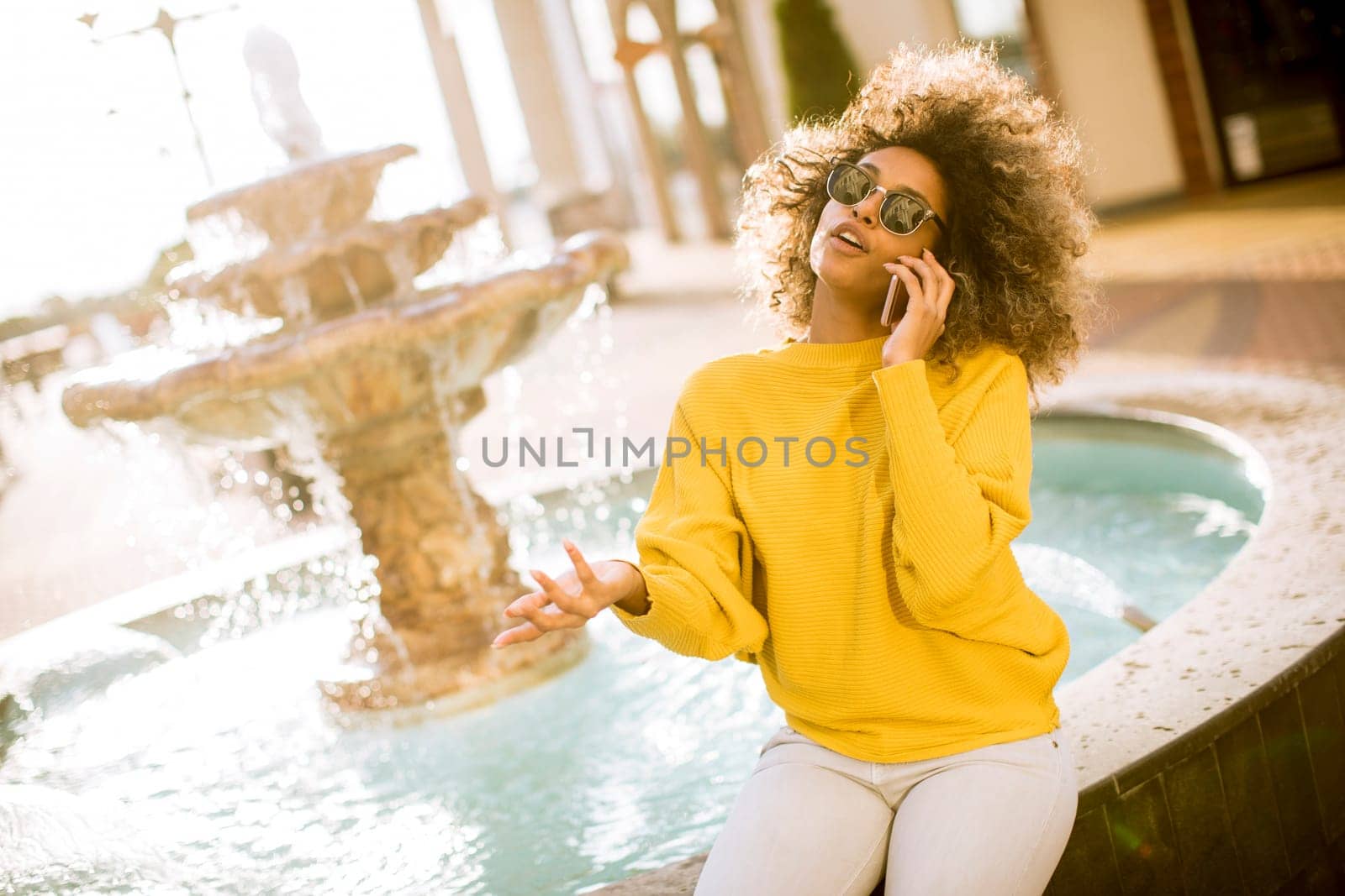 Aftican american young woman sits near fountain and talks on smartphone