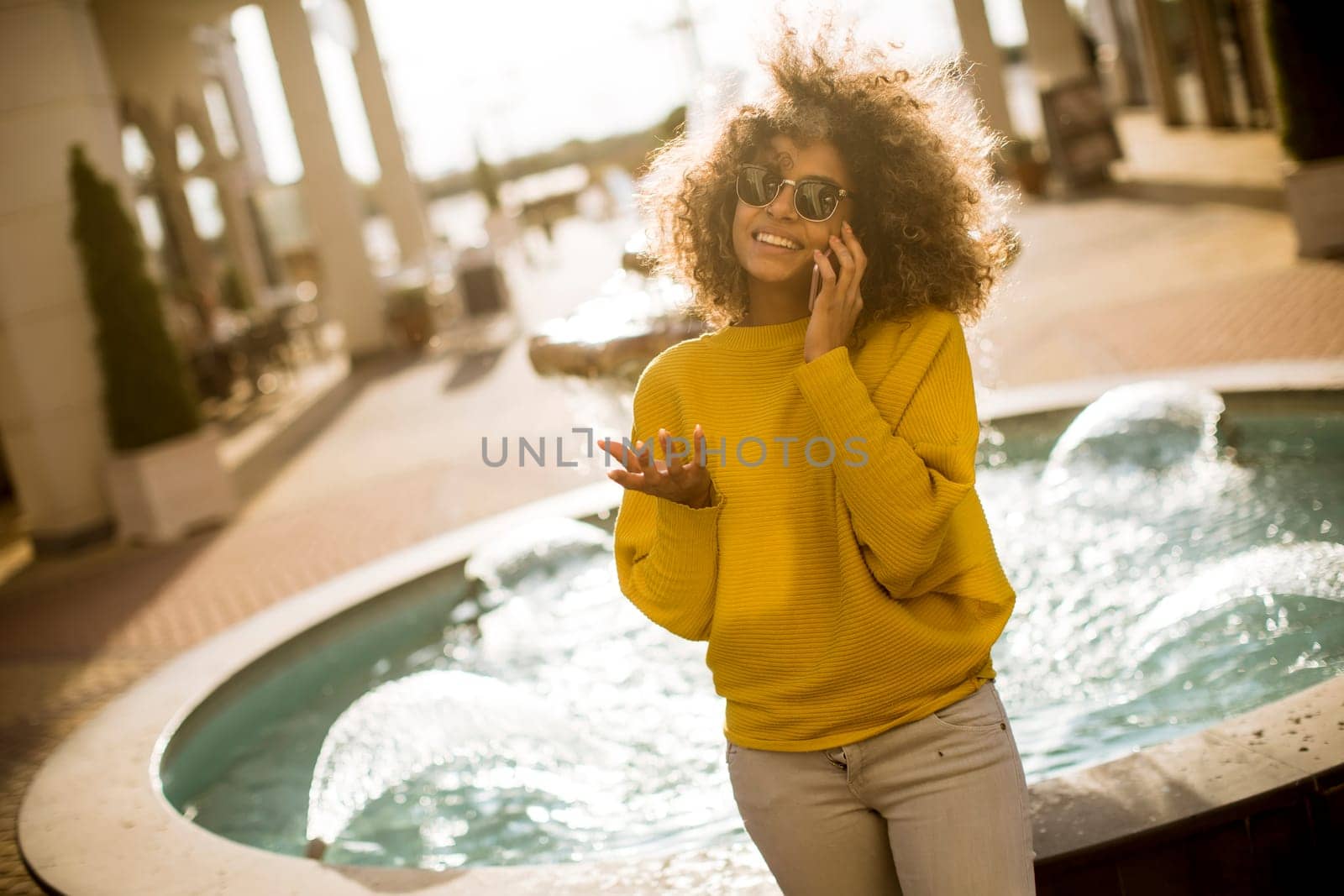 Attractive young woman with curly hair using her touch screen mobile cell phone by the fountain