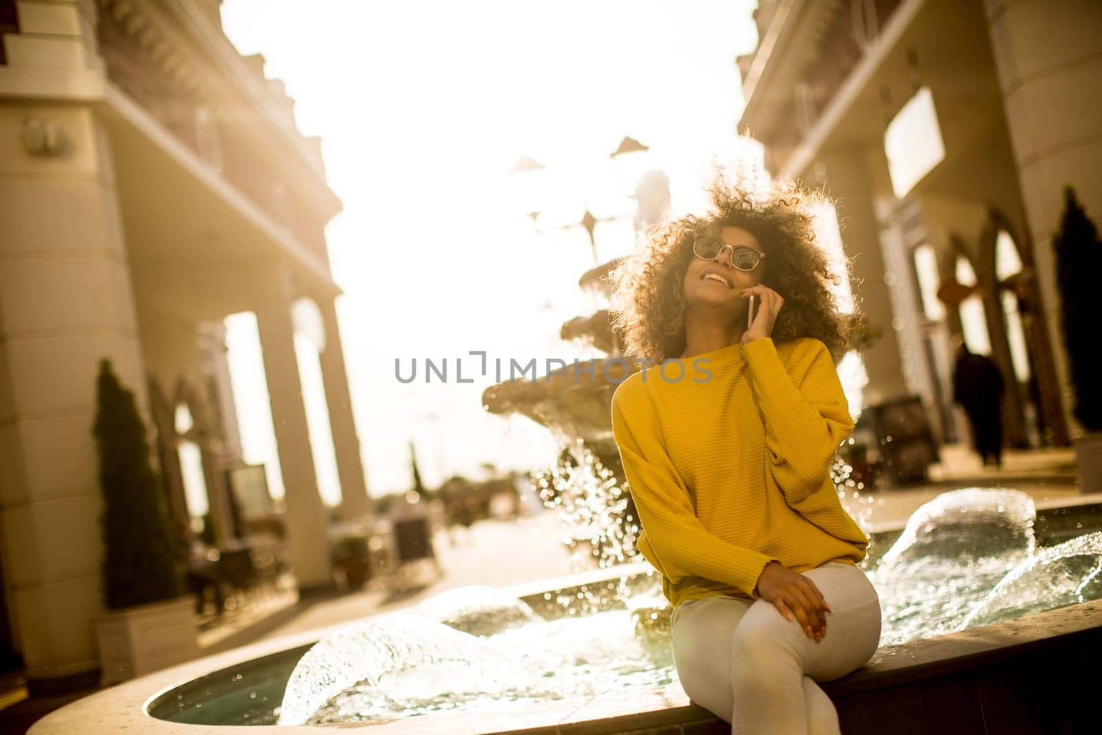 Attractive young woman with curly hair using her touch screen mobile cell phone by the fountain