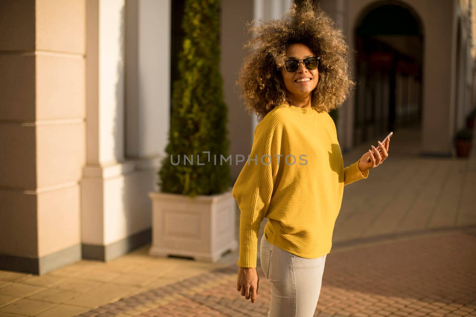 Attractive young woman with curly hair using her touch screen mobile cell phone on the street