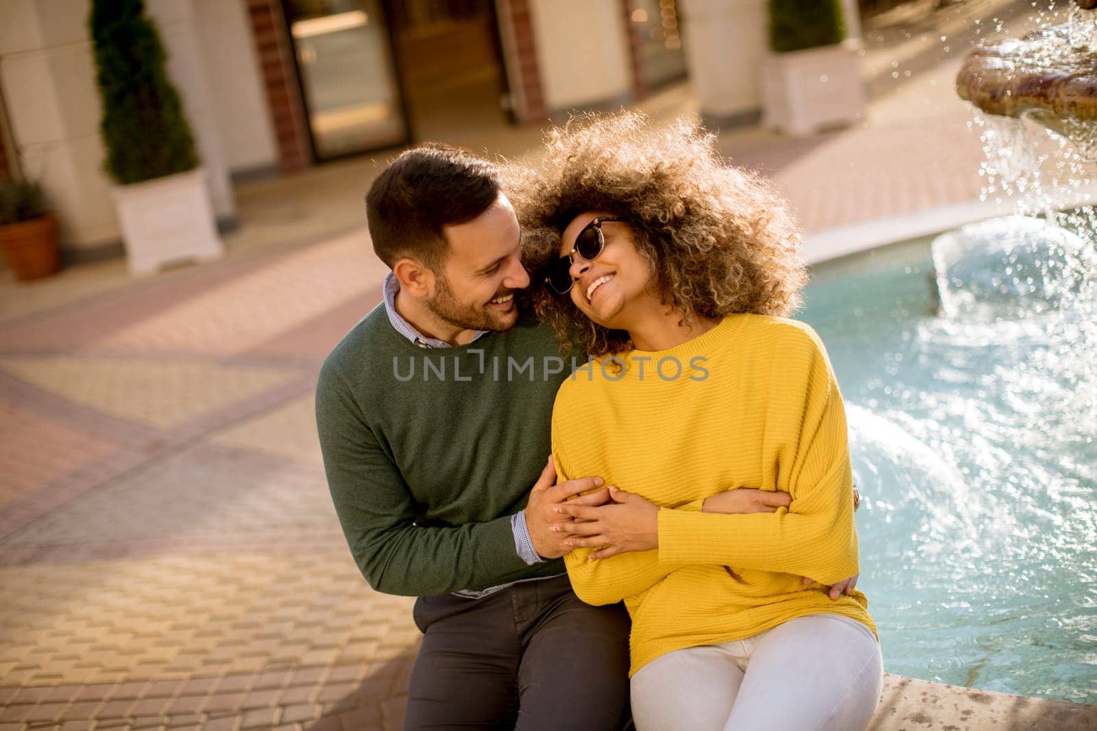 Portrait of beautiful smiling love couple sitting near fountain on a sunny day