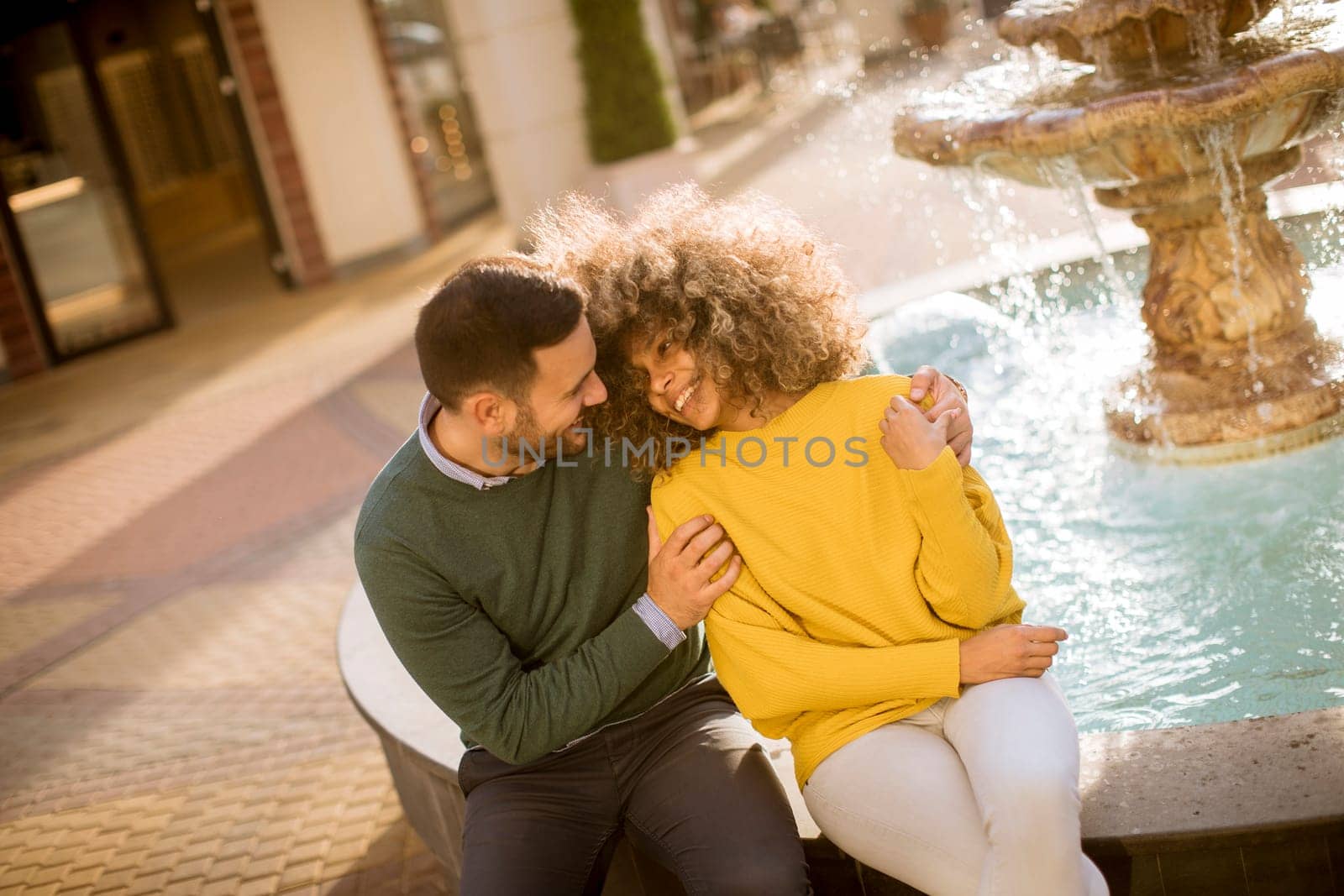 Portrait of beautiful smiling love couple sitting near fountain on a sunny day