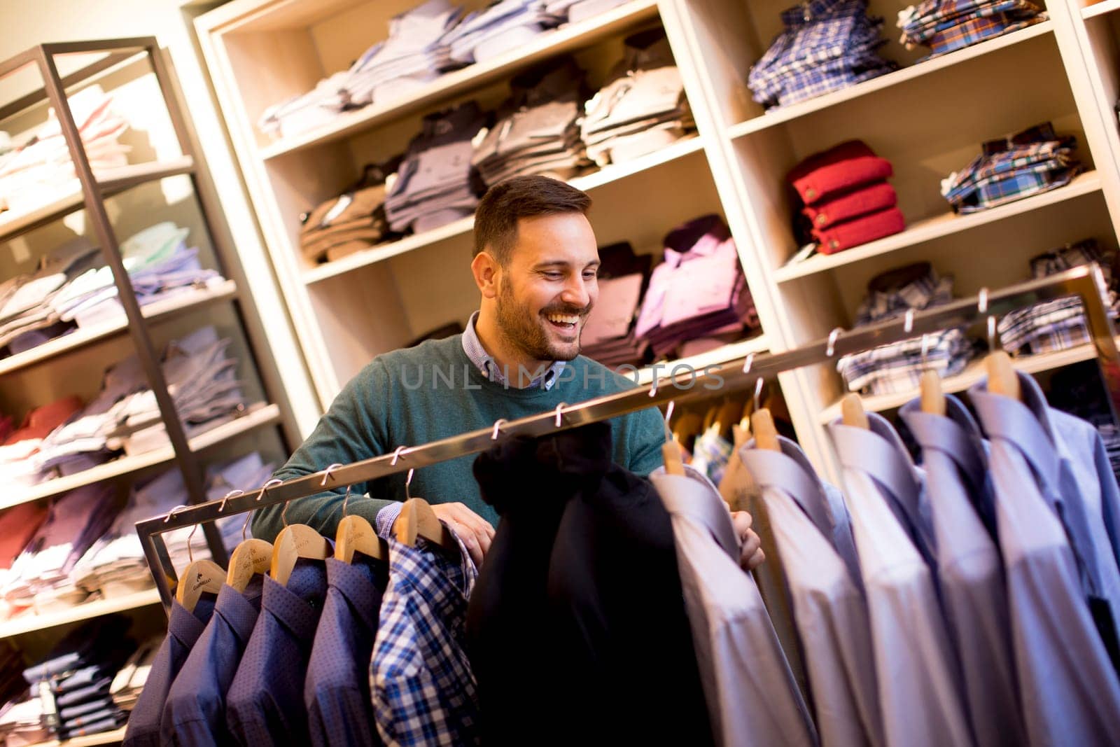Portrait of a young cheerfull man looking at clothes to buy at shop