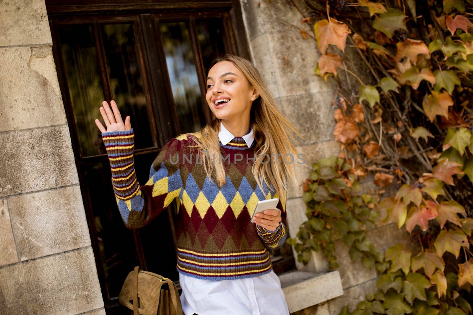 Pretty young woman standing with mobile phone on street at sunny autumn day