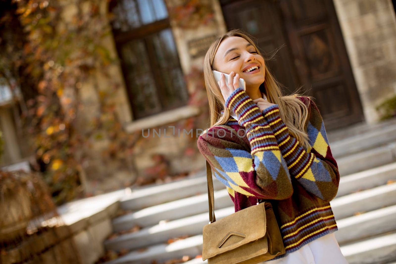 Pretty young woman standing with mobile phone on street at sunny autumn day