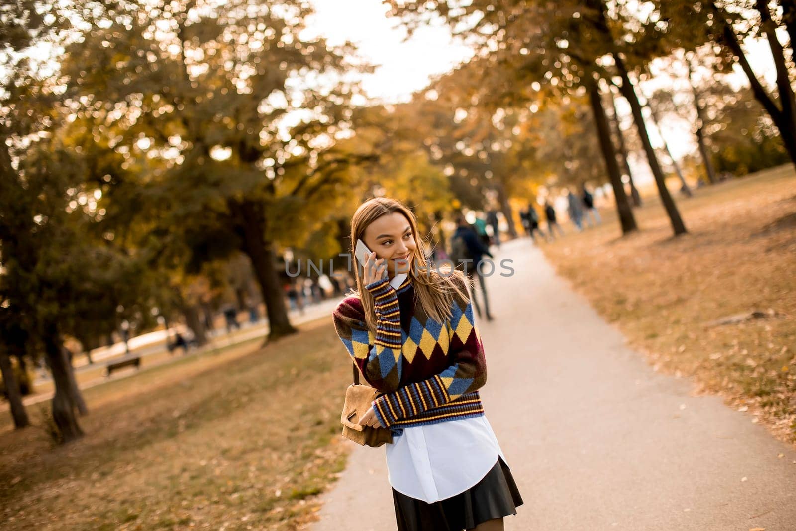 Pretty young woman walking in the autumn park and using a mobile phone