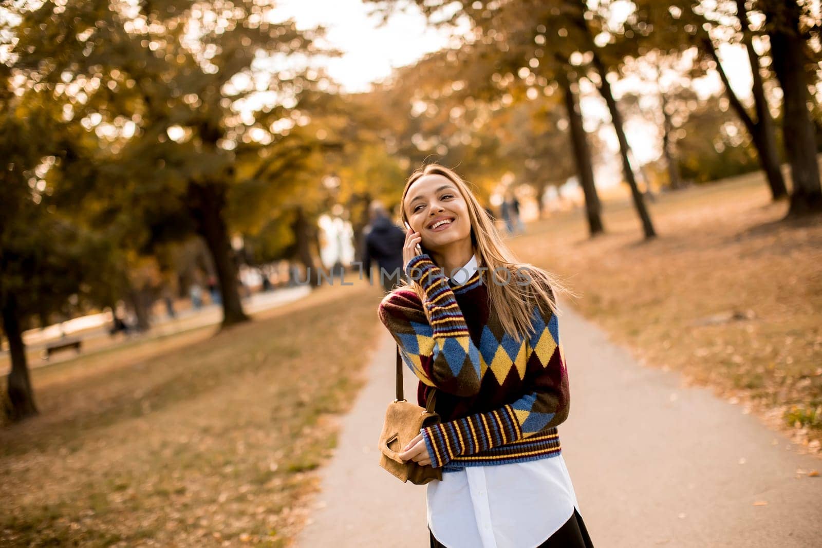 Pretty young woman walking in the autumn park and using a mobile phone