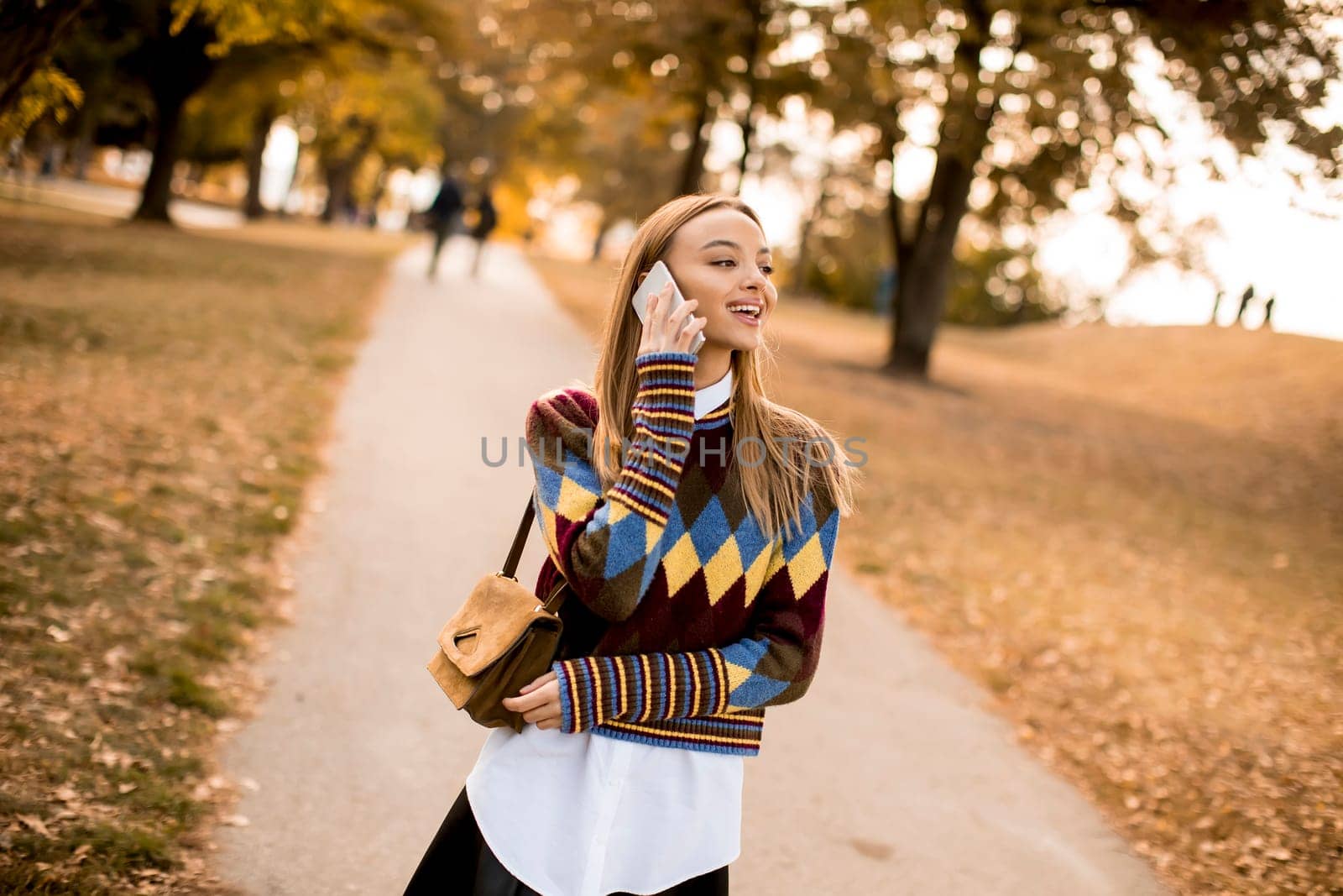 Pretty young woman walking in the autumn park and using a mobile phone