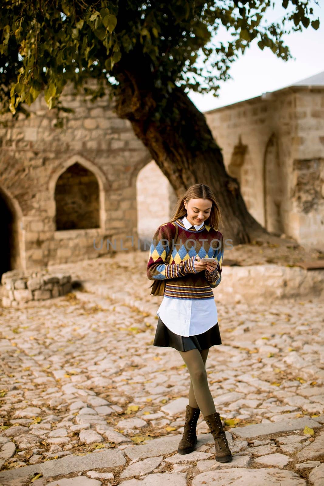 Pretty young woman standing with mobile phone on street at sunny autumn day