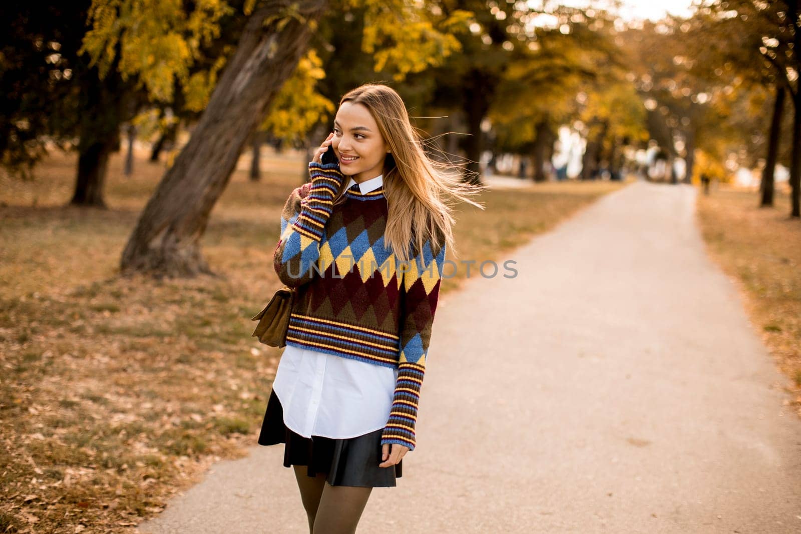 Pretty young woman walking in the autumn park and using a mobile phone