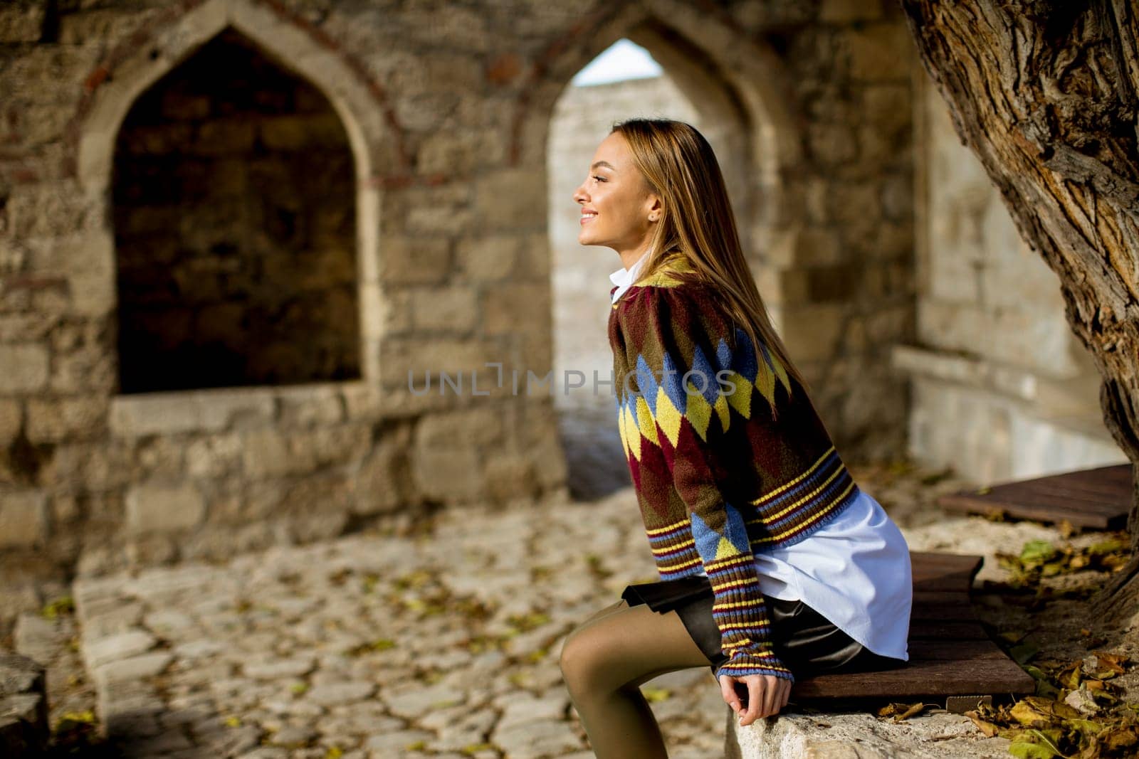 Pretty young woman sitting on the bench watching yellow leaves tree in the autumn park