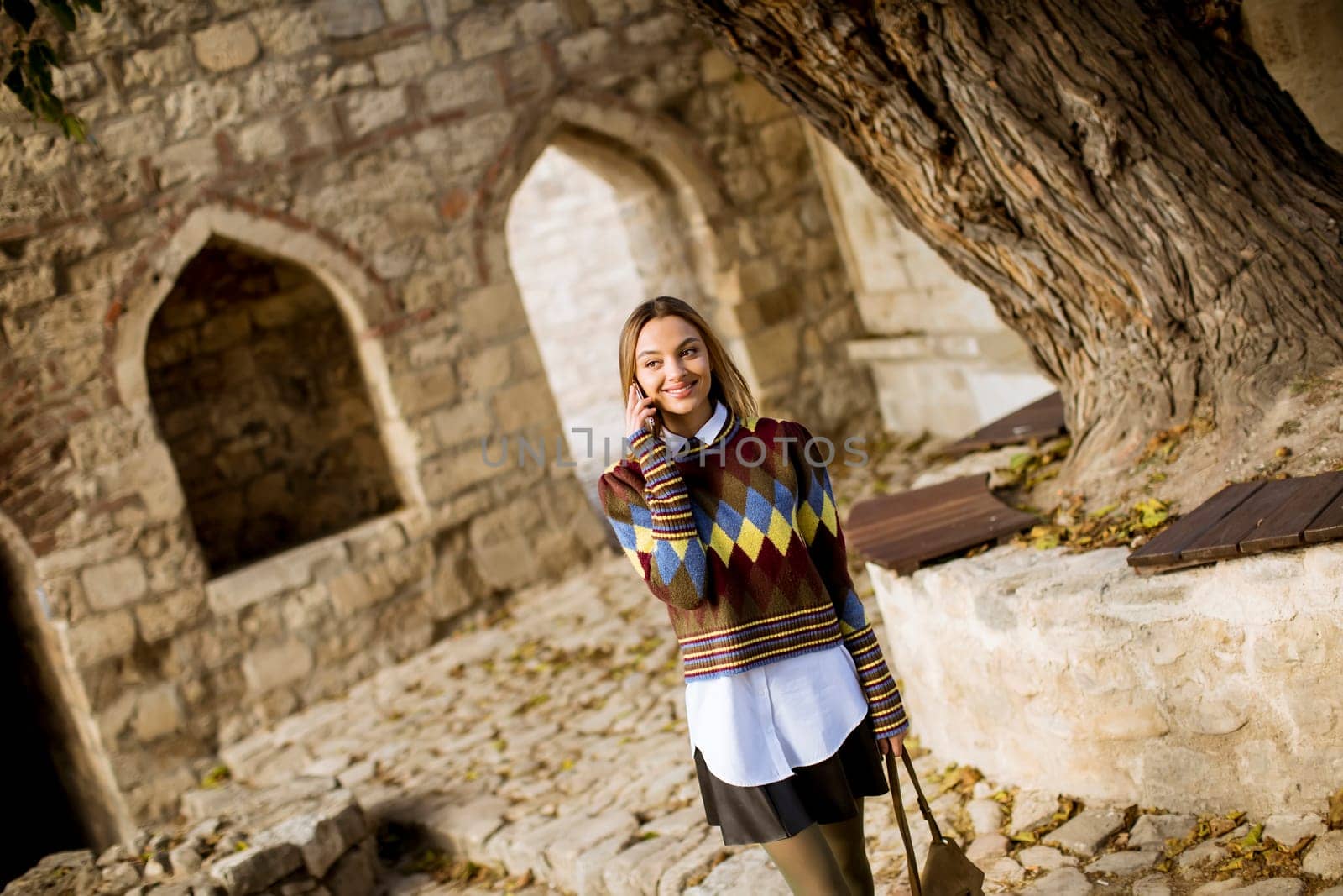 Pretty young woman walking in the autumn park and using a mobile phone
