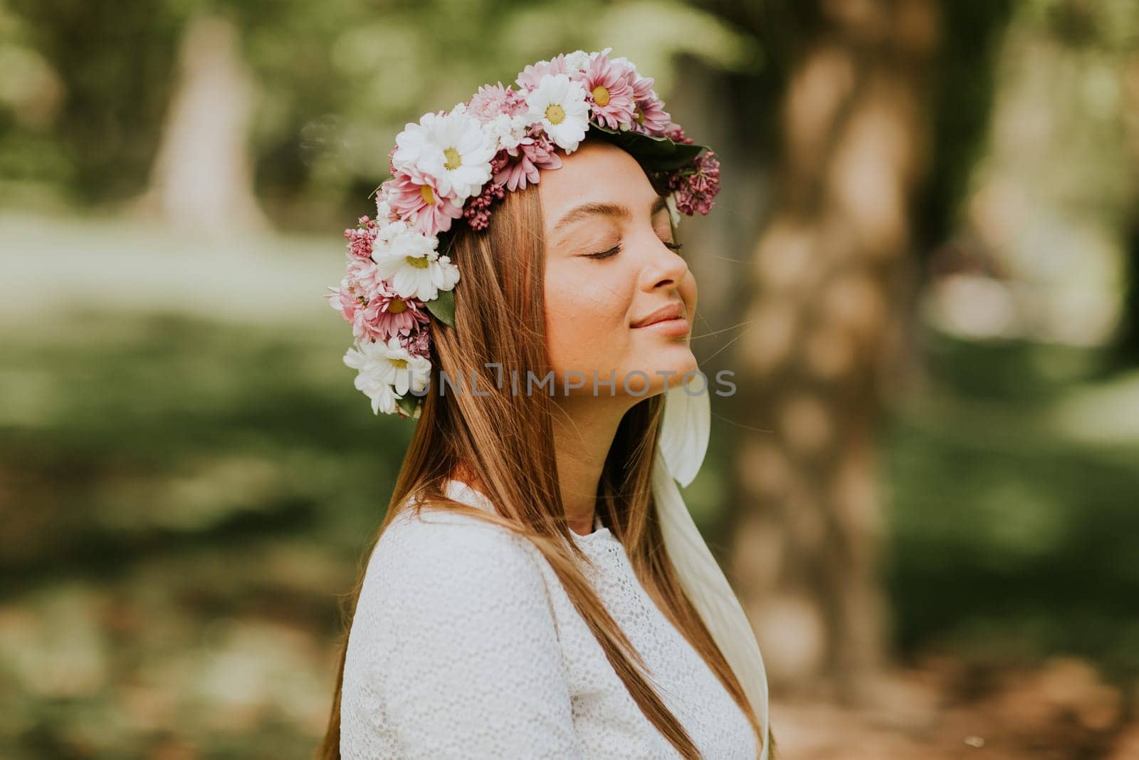 Portrait of young woman with wreath of fresh flowers on head in the park